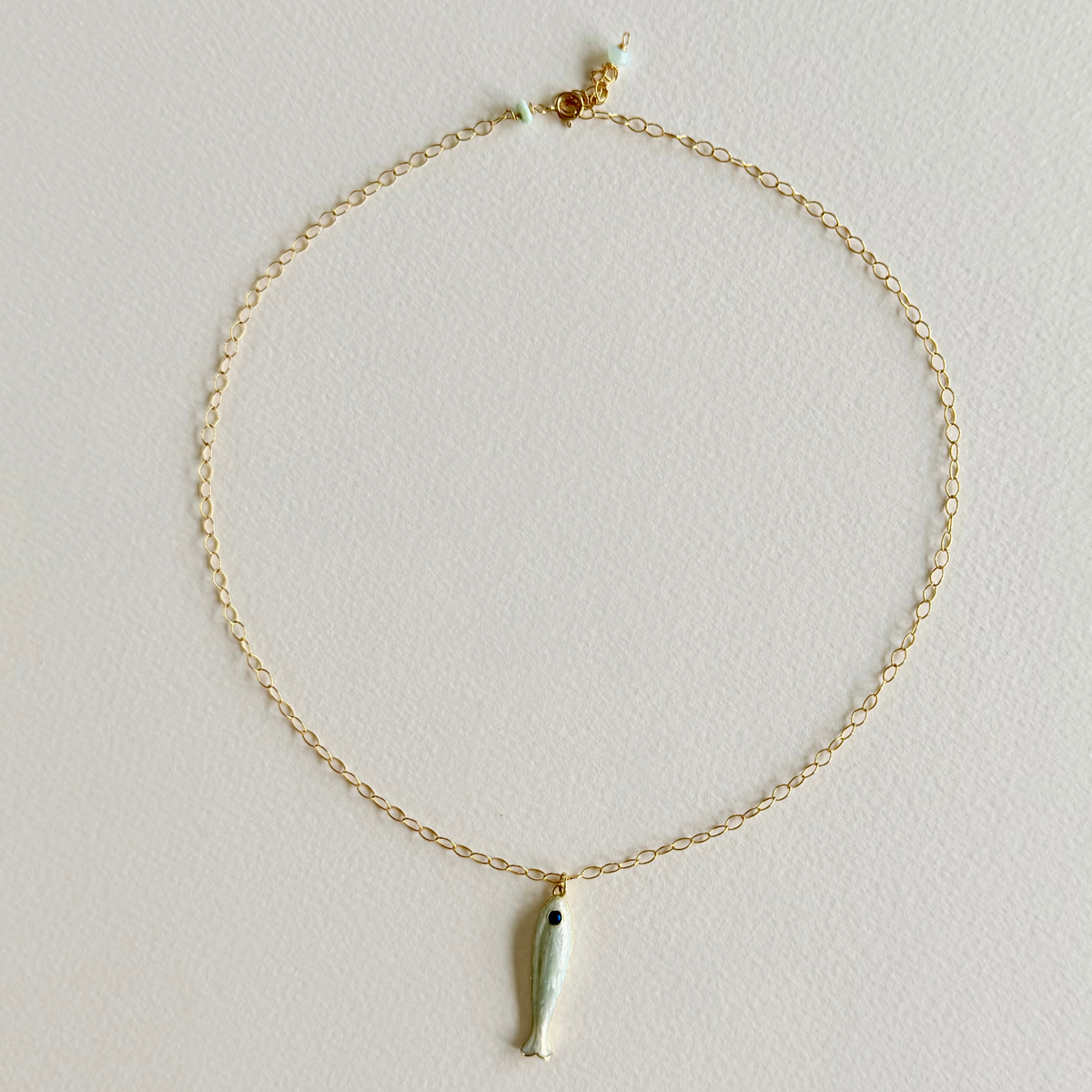 Gold necklace with a small pendant on a light gray background