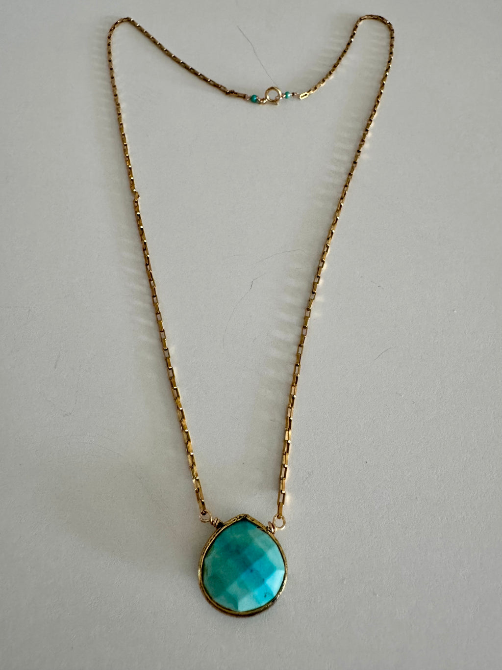 Entire turquoise pendant gold chain necklace on textured white background. Two turquoise beads offset the clasp.