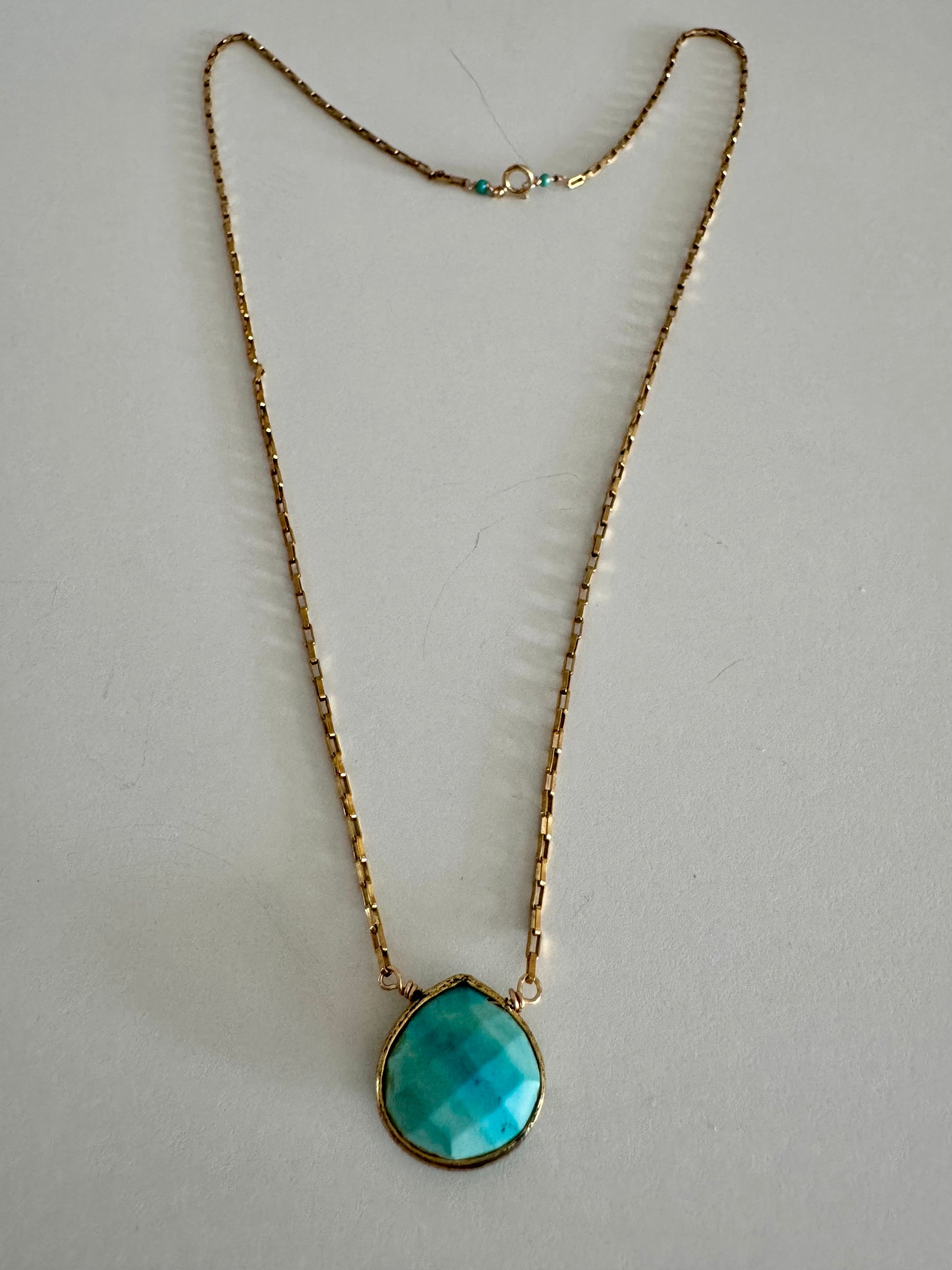 Entire turquoise pendant gold chain necklace on textured white background. Two turquoise beads offset the clasp.