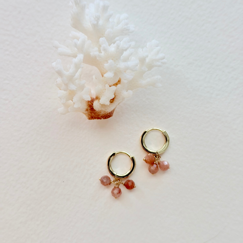 Gold hoop earrings with pink gemstones on a white coral background