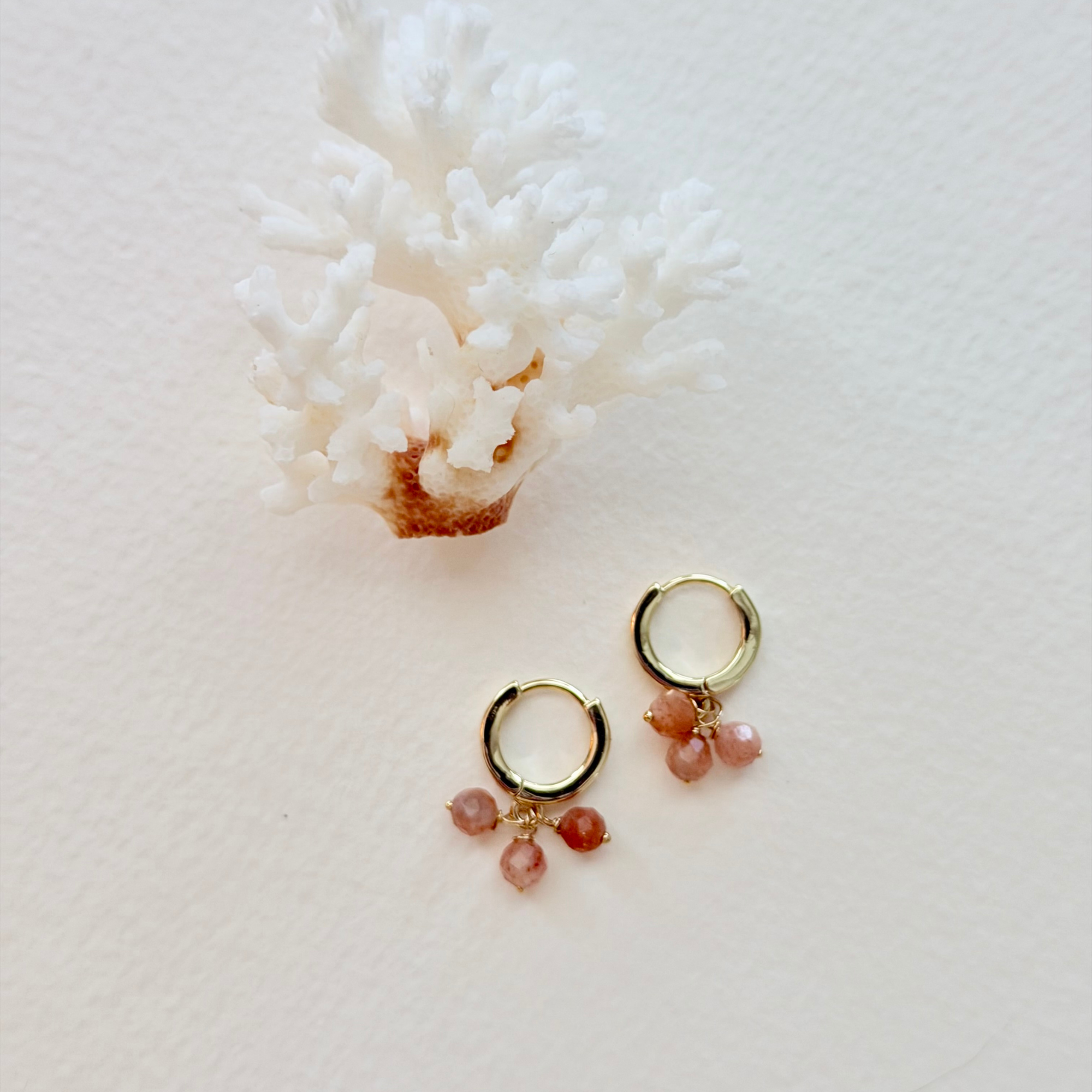 Gold hoop earrings with pink gemstones on a white coral background