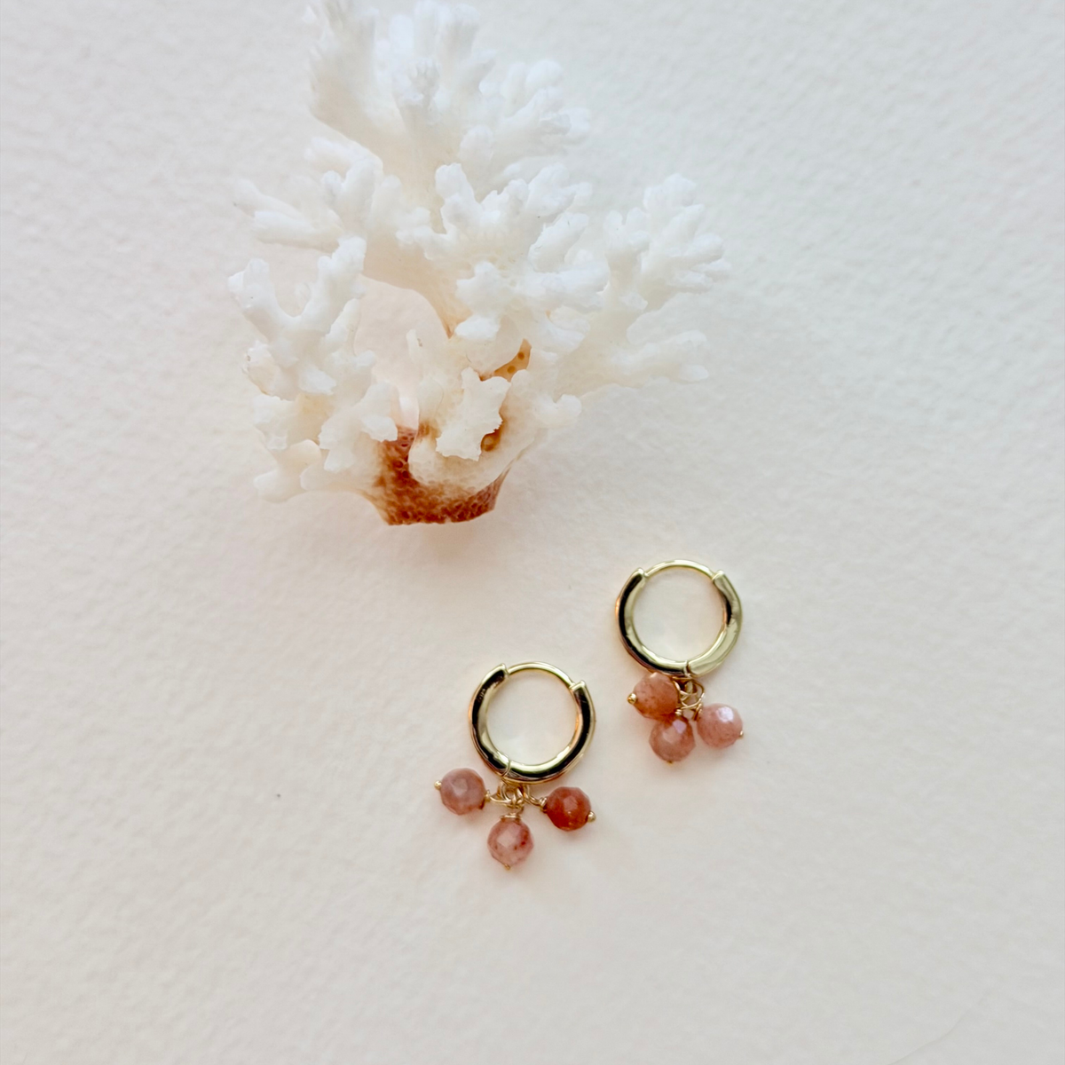 Gold hoop earrings with pink gemstones on a white coral background