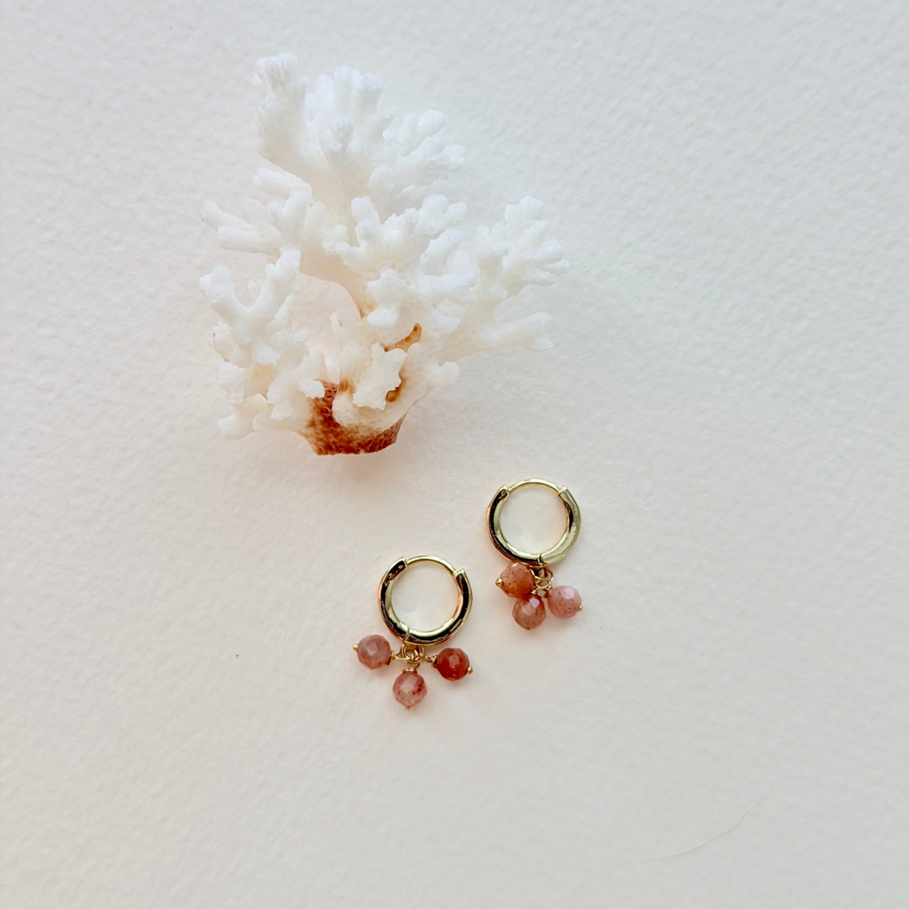 Gold hoop earrings with pink gemstones on a white background