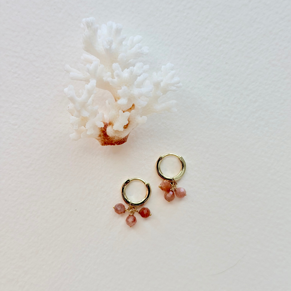 Gold hoop earrings with pink gemstones on a white background