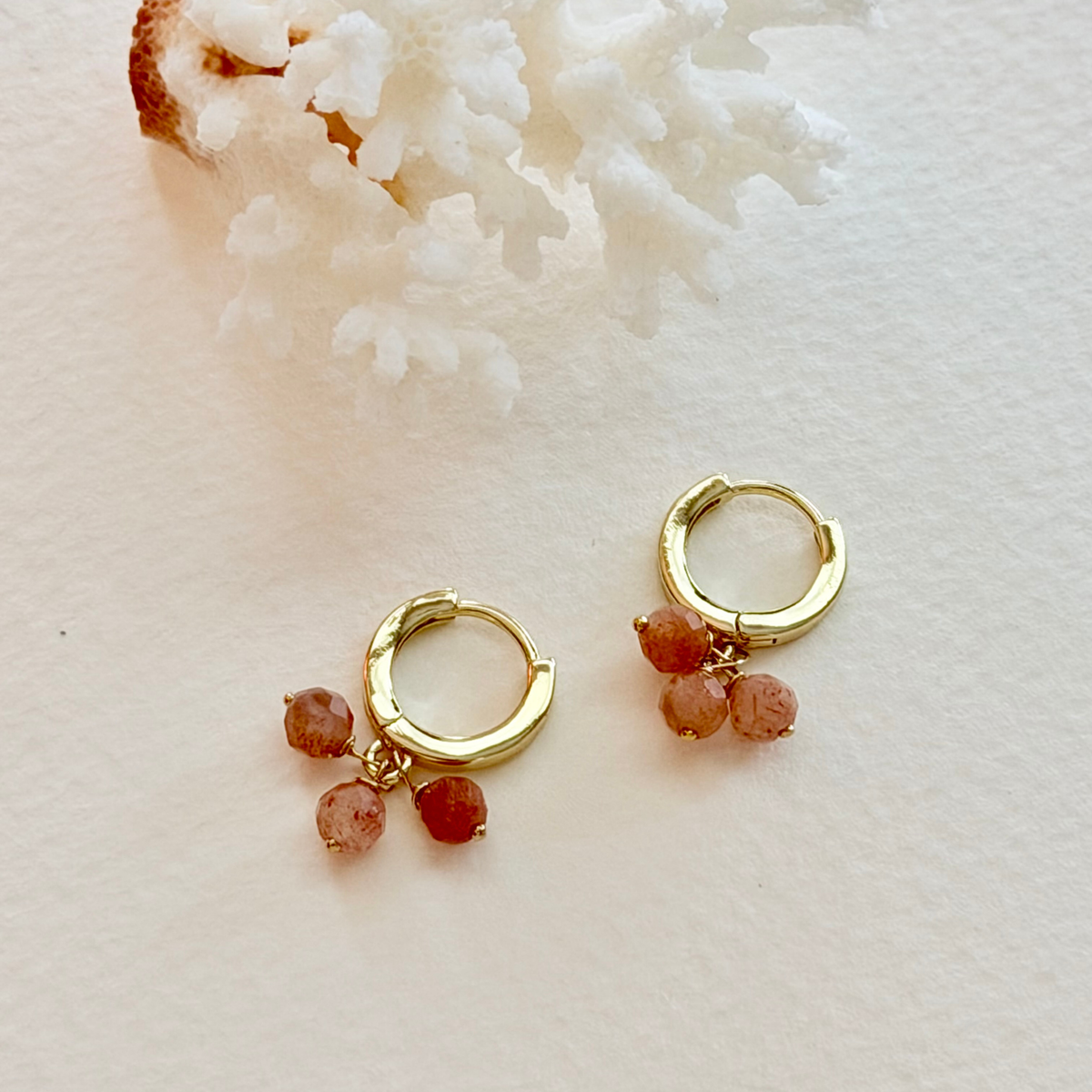 Gold hoop earrings with red beads on a light background