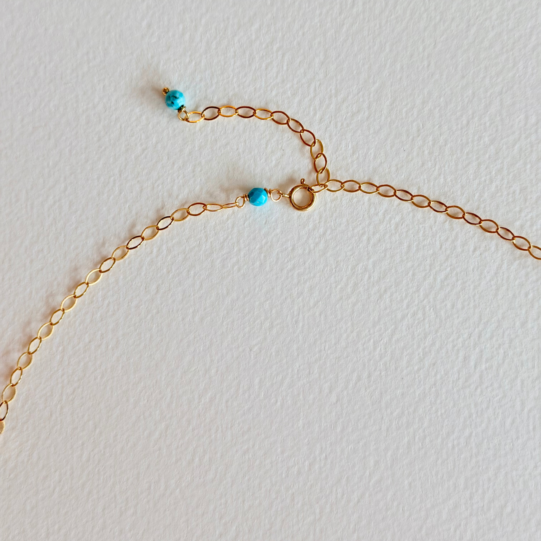 Gold chain necklace with turquoise beads close up of clasp on a light gray background