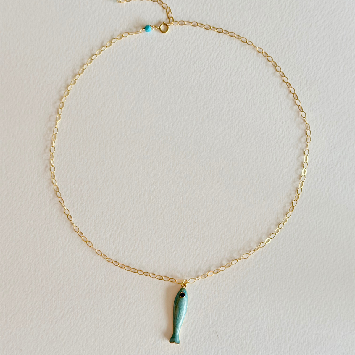 Gold necklace with a turquoise fish pendant on a light gray background