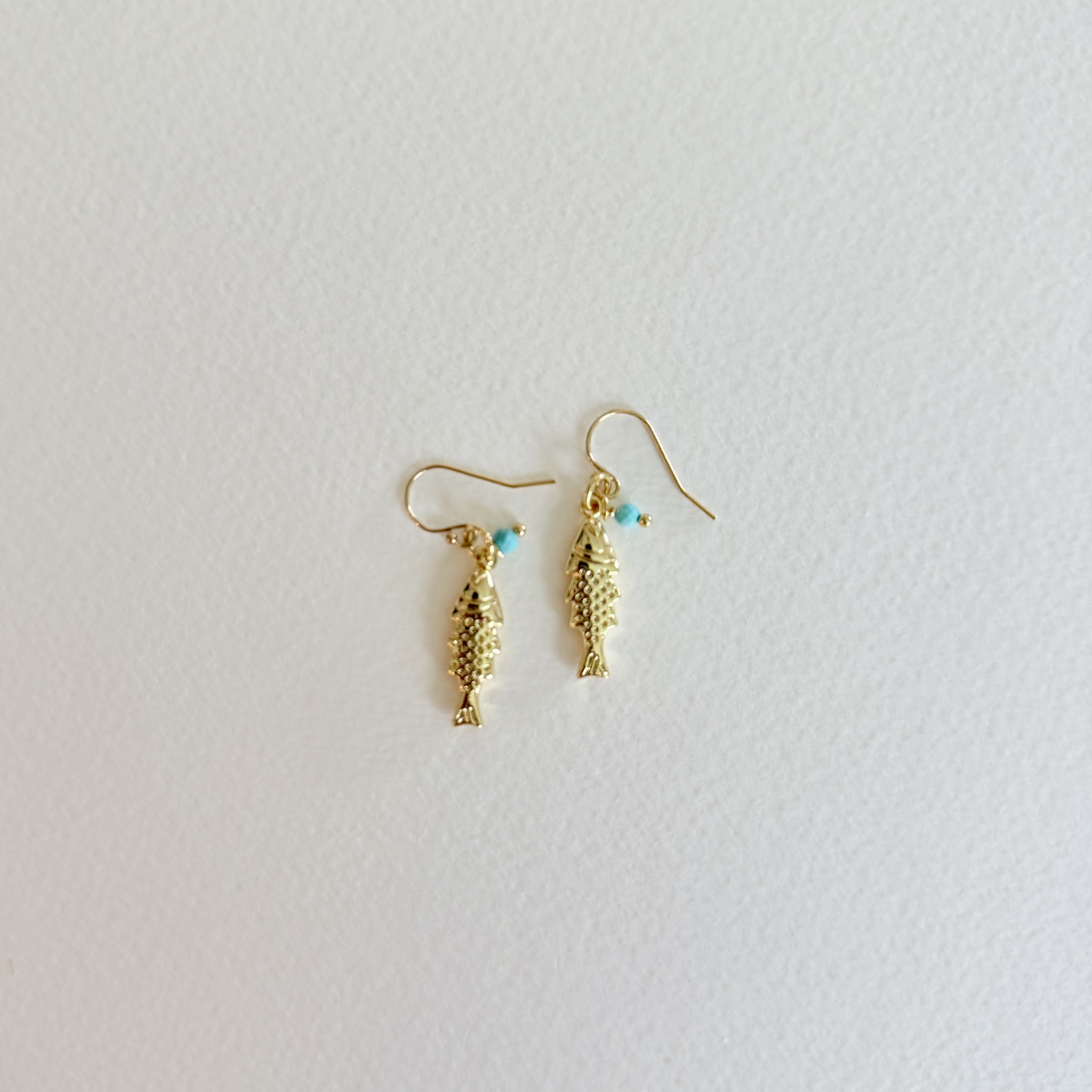 Gold fish-shaped earrings with turquoise beads on a light gray background