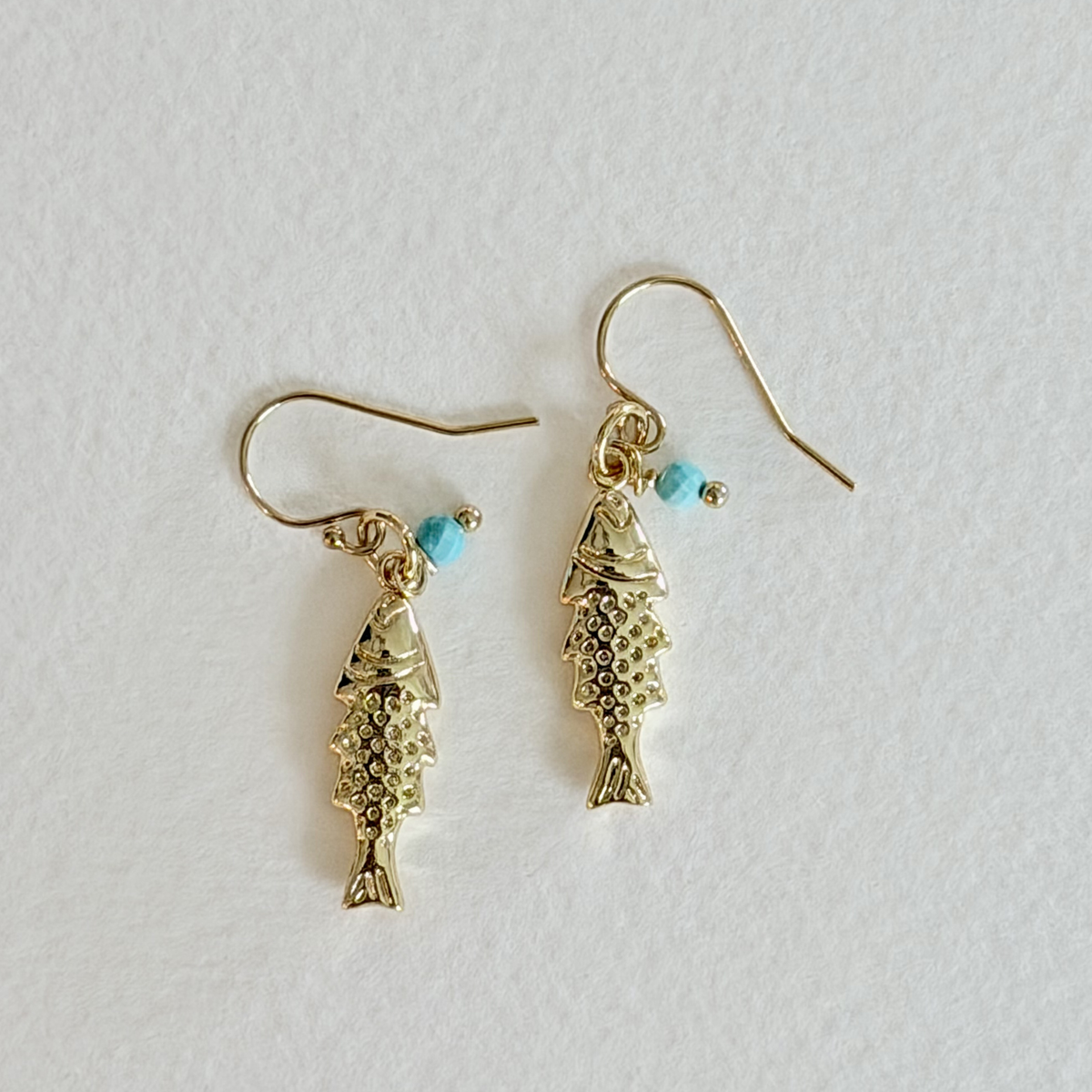 Gold fish-shaped earrings with turquoise beads on a light gray background