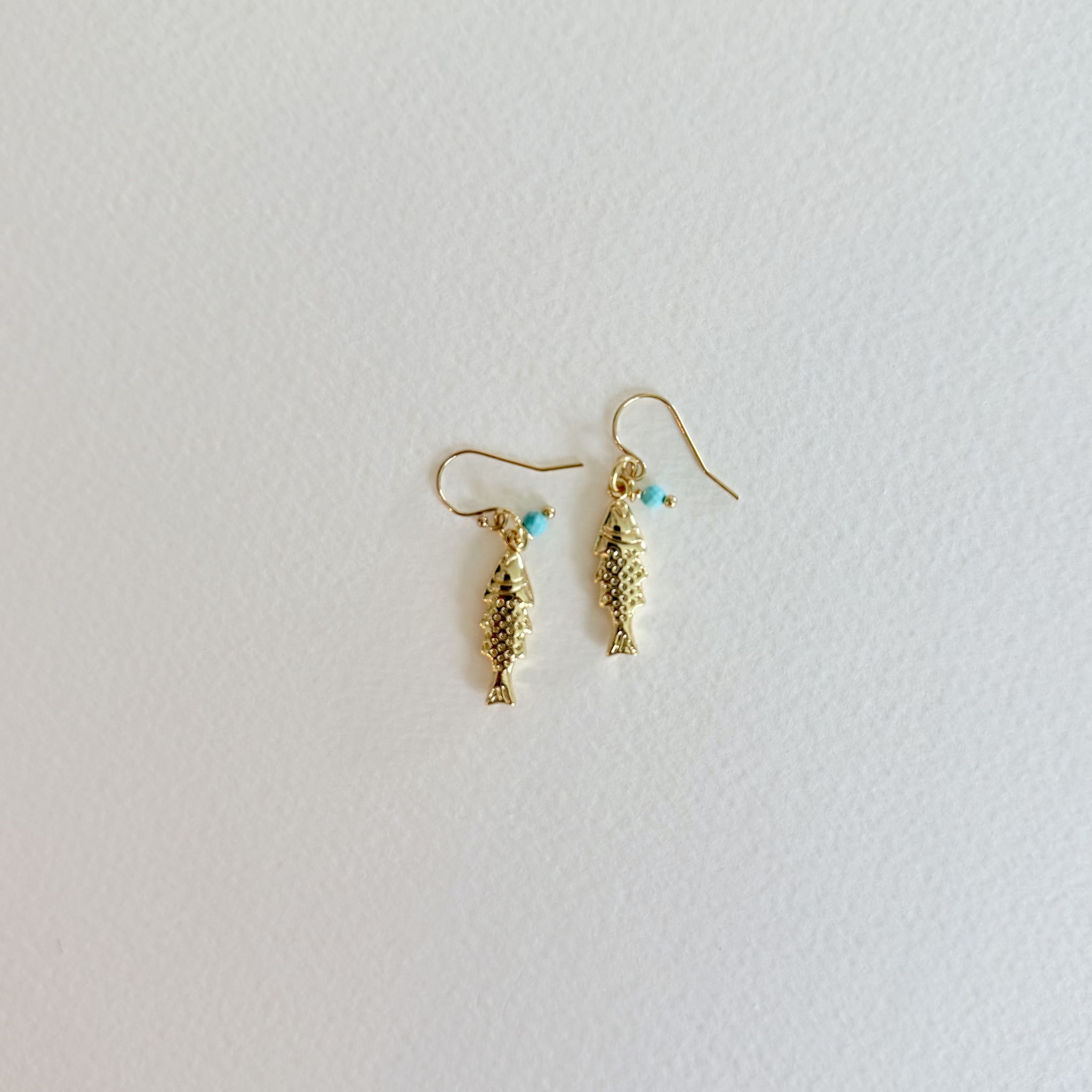 Gold fish-shaped earrings with turquoise beads on a light gray background