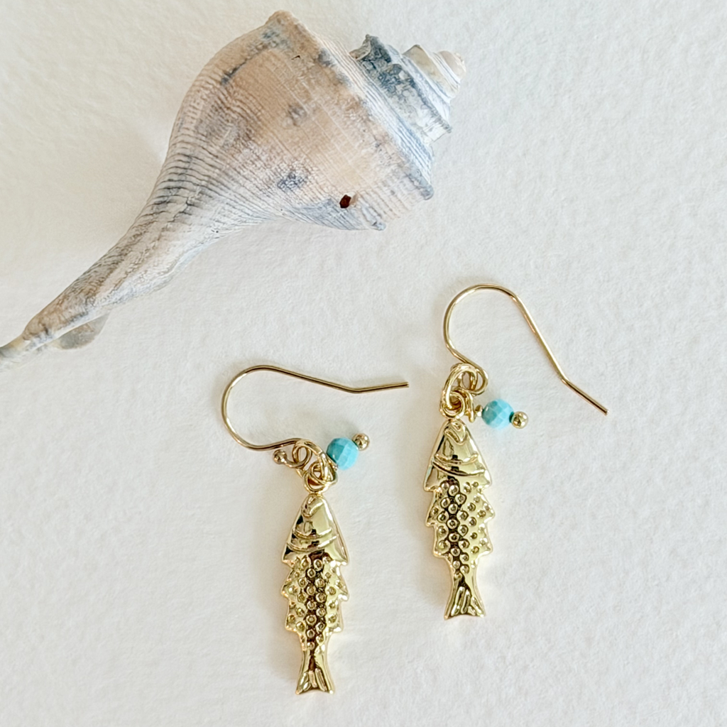 Gold fish-shaped earrings with turquoise beads on a white background with a shell.