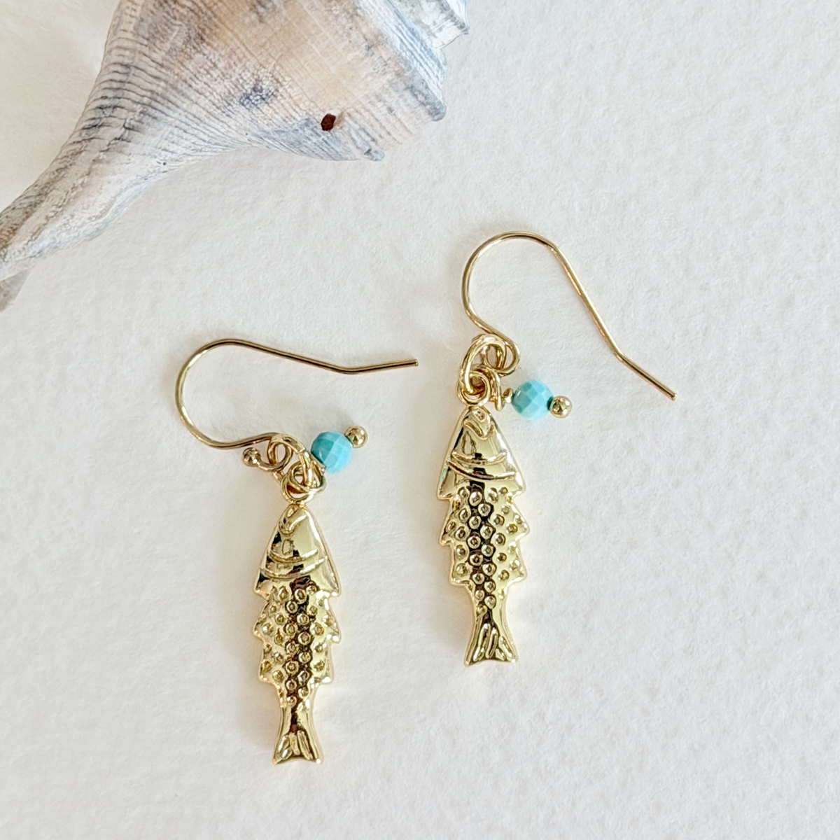 Gold fish-shaped earrings with turquoise beads on a white background