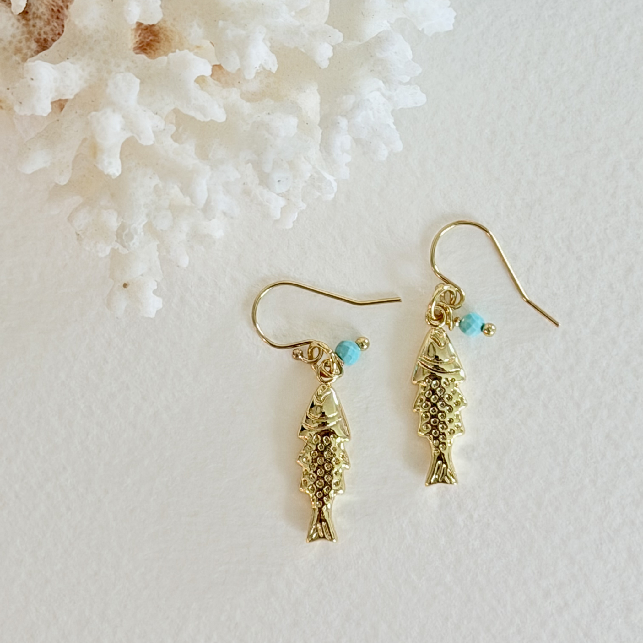 Gold fish-shaped earrings with turquoise beads on a light background