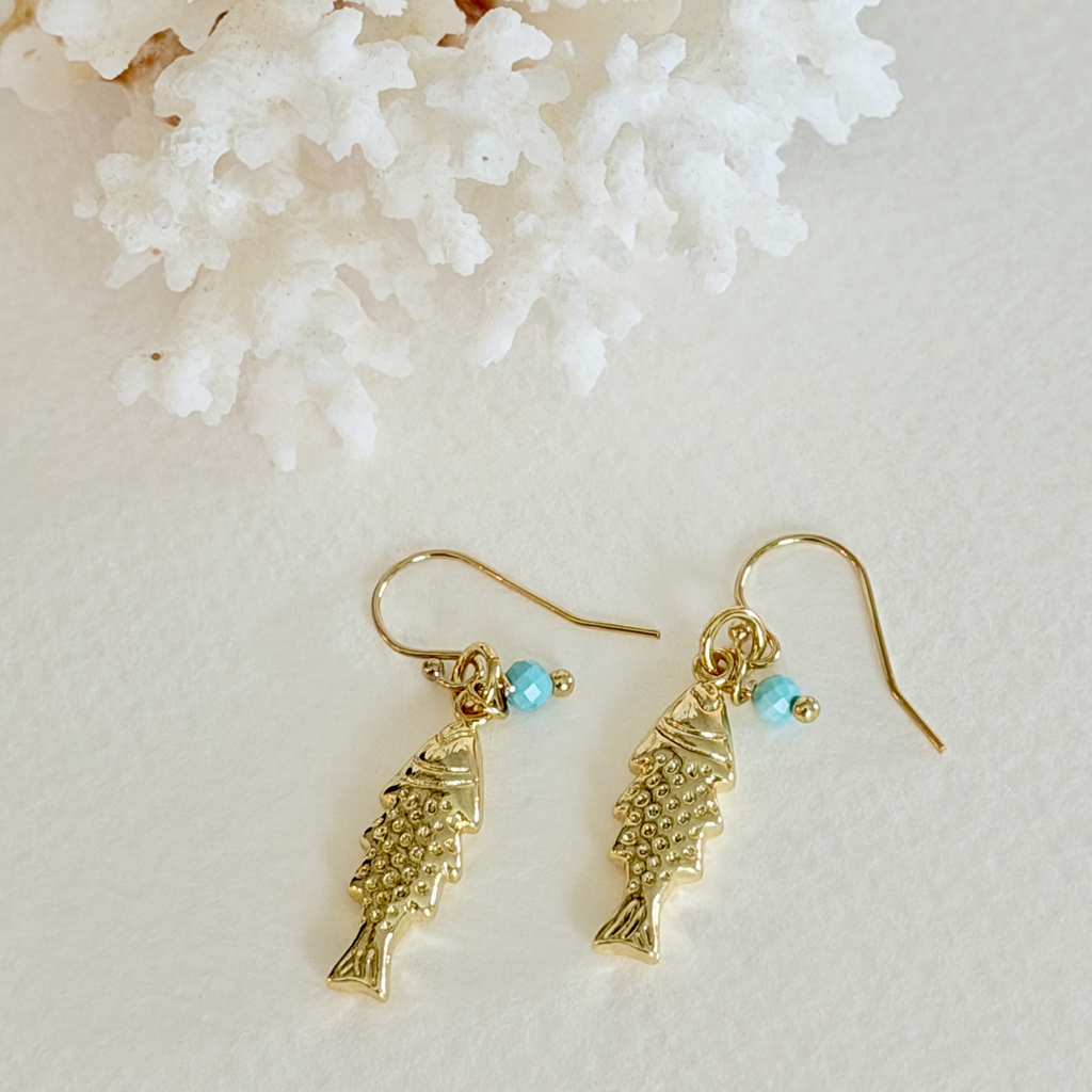 Gold fish-shaped earrings with turquoise beads on a light background