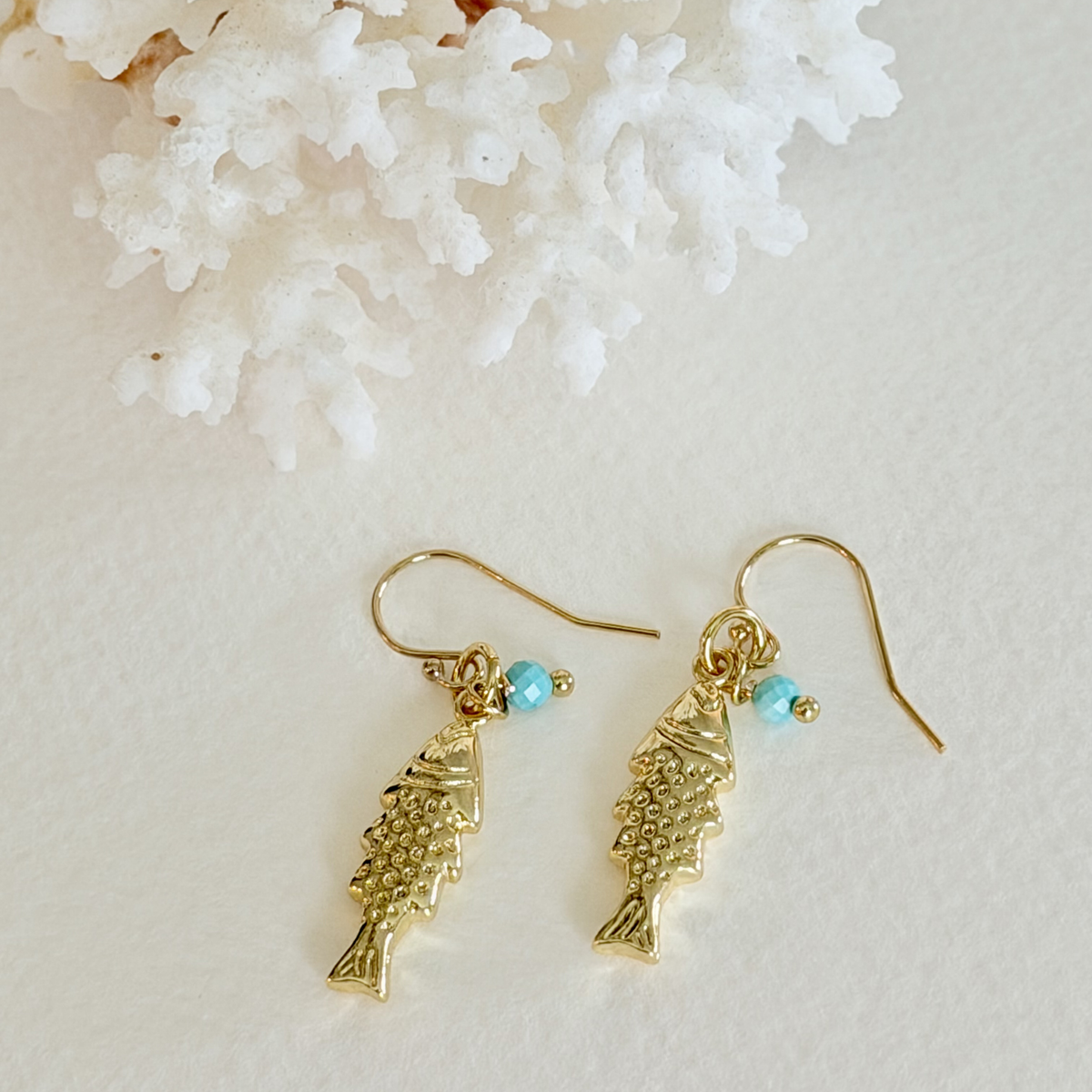 Gold fish-shaped earrings with turquoise beads on a light background