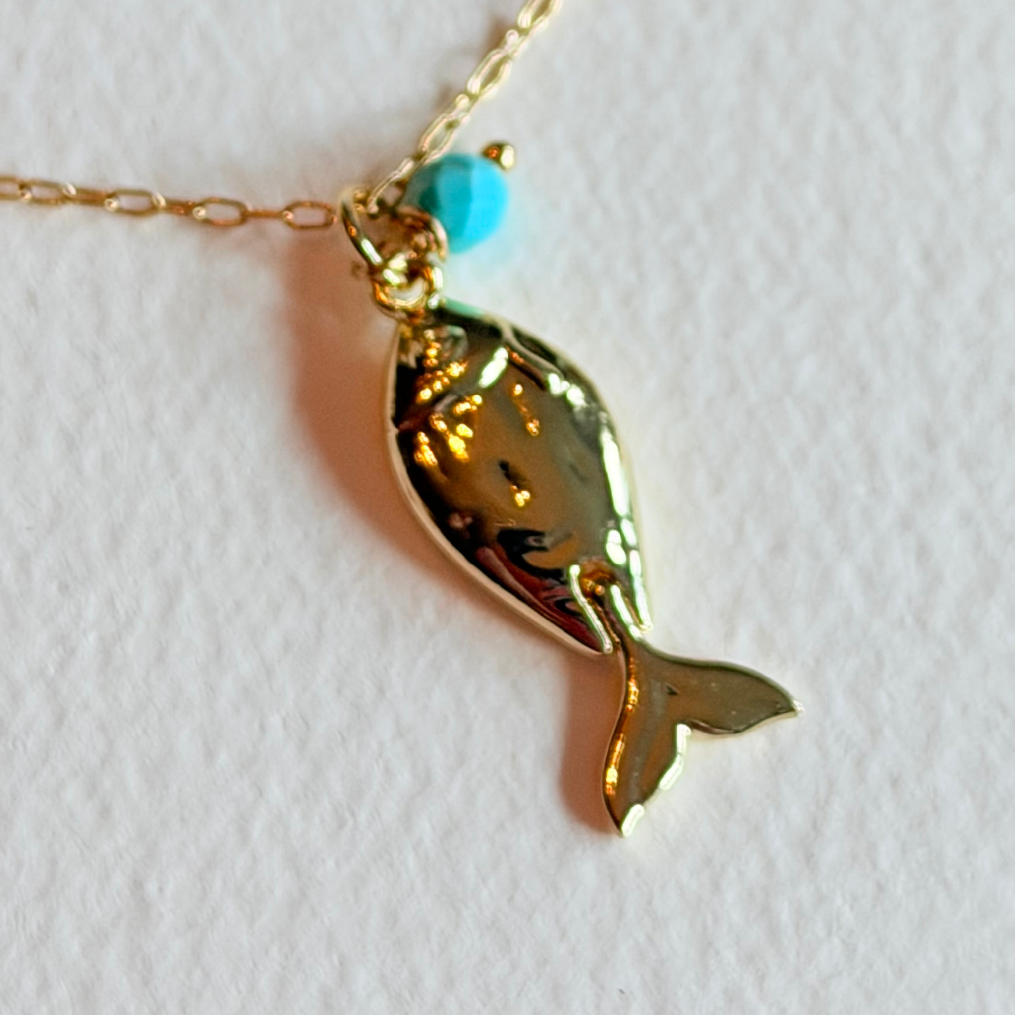 Gold fish-shaped pendant with a turquoise bead on a white background