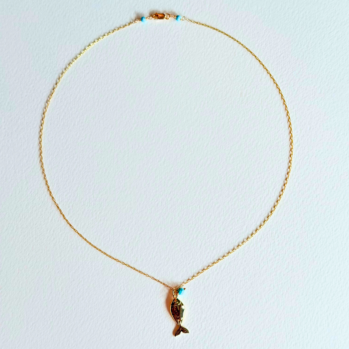 Gold necklace with a fish pendant on a light blue background