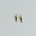 Gold fish-shaped earrings on a light gray background