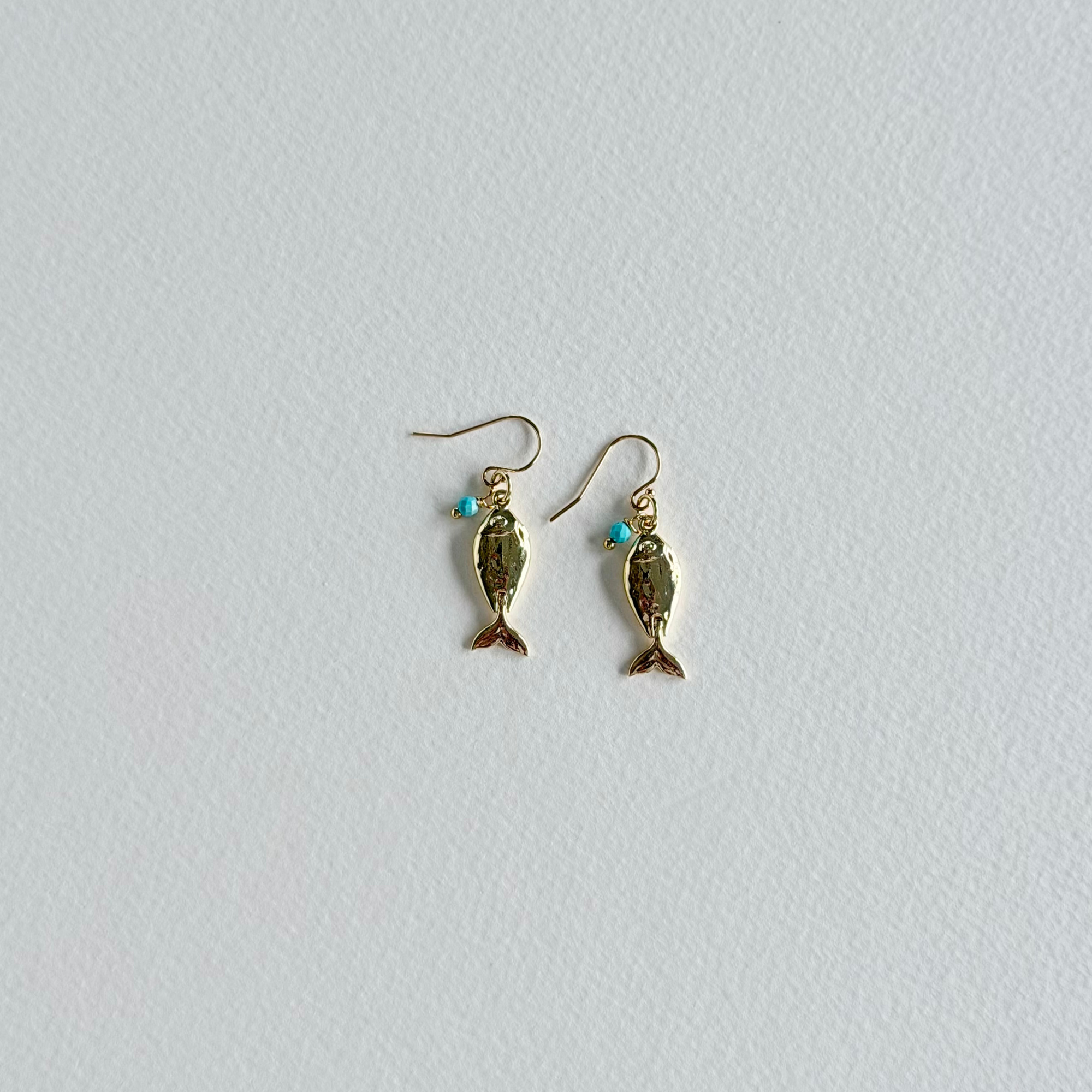 Gold fish-shaped earrings on a light gray background