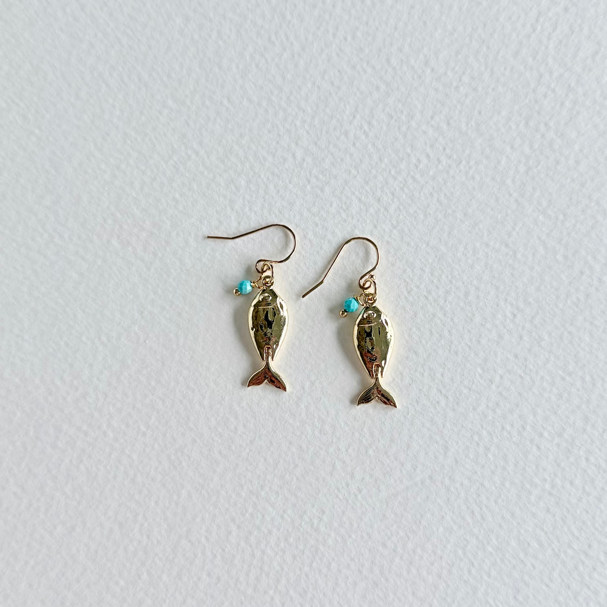 Gold fish-shaped earrings with turquoise beads on a light gray background