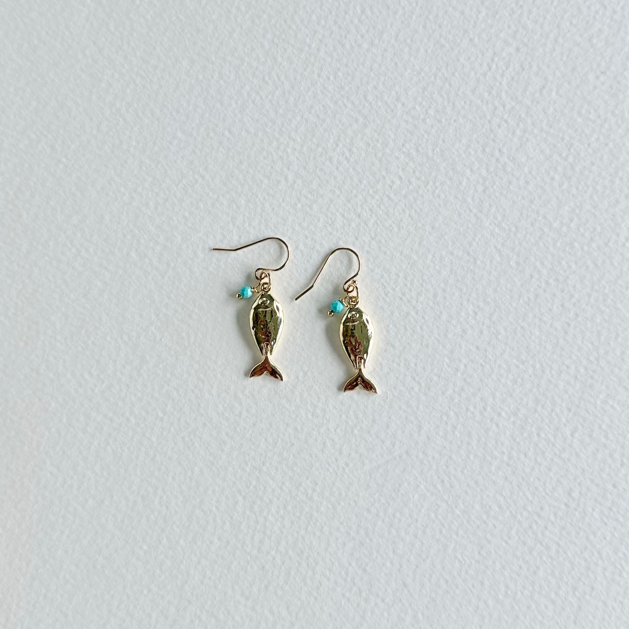 Gold fish-shaped earrings with turquoise stones on a light gray background