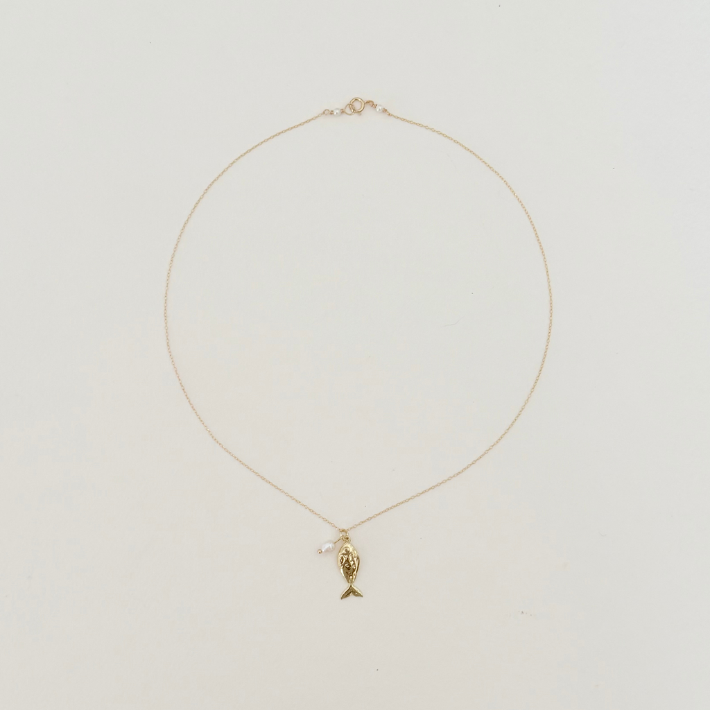 Delicate fish pendant on a gold chain displayed on a light grey background.