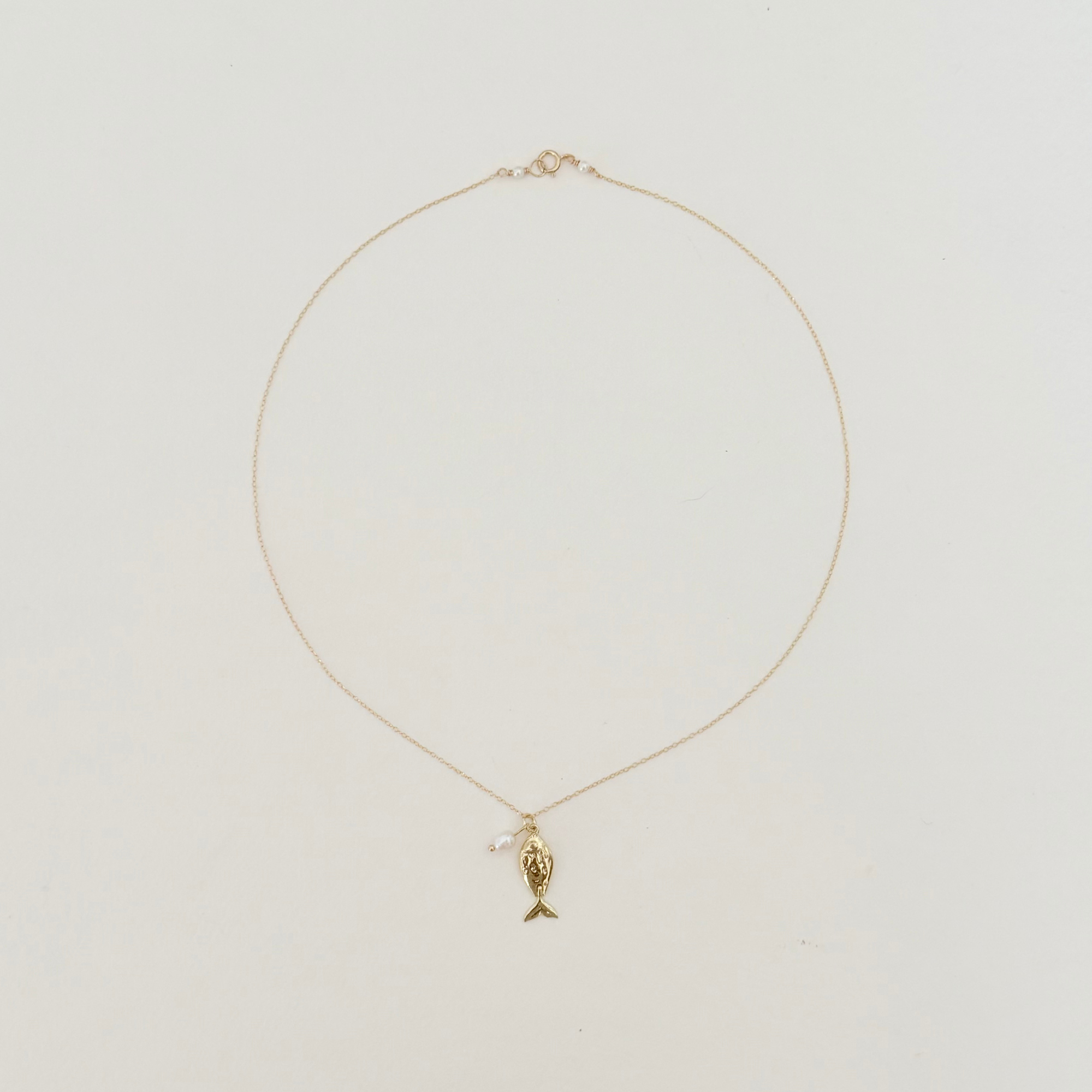 Delicate fish pendant on a gold chain displayed on a light grey background.