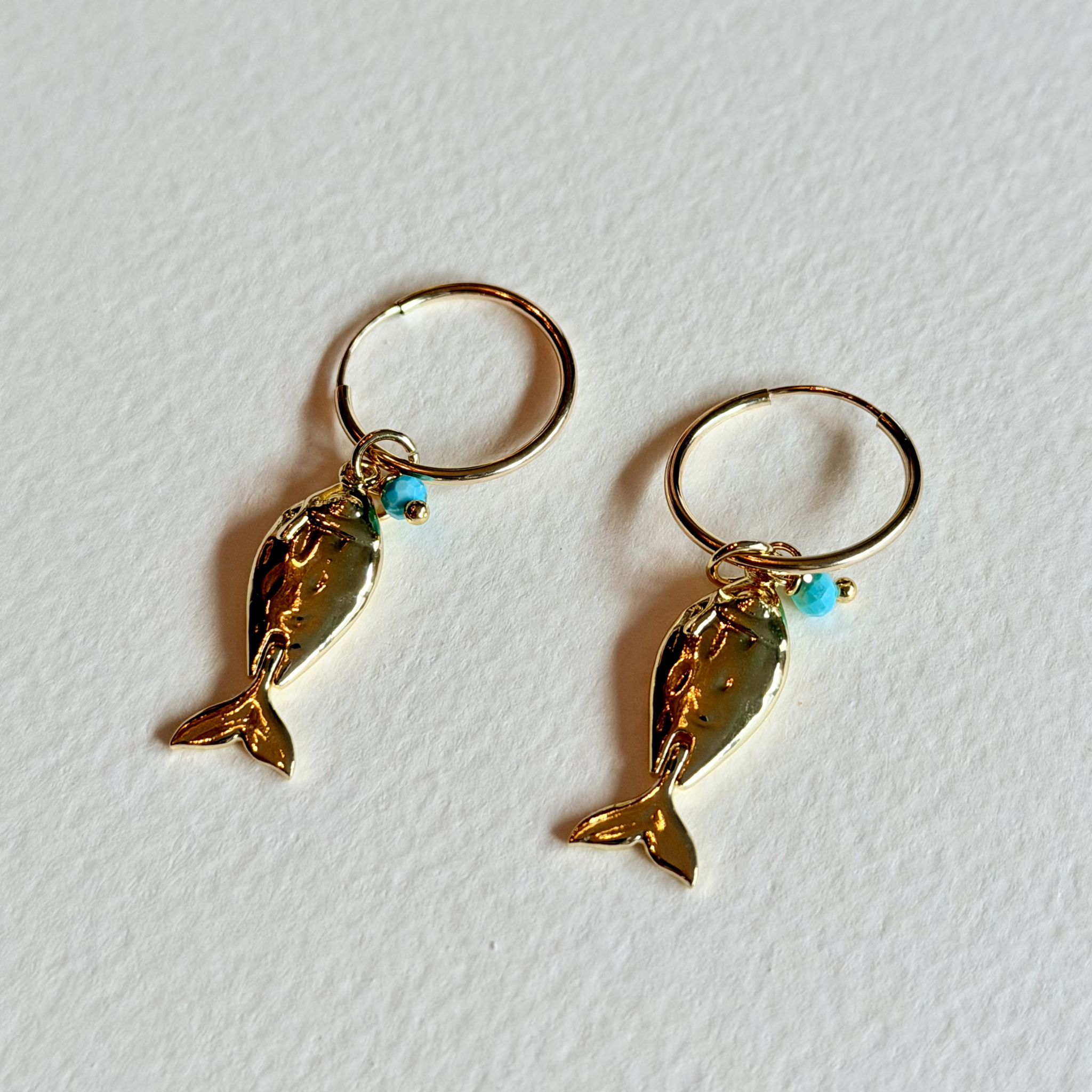 Gold fish-shaped earrings with turquoise beads on a white background