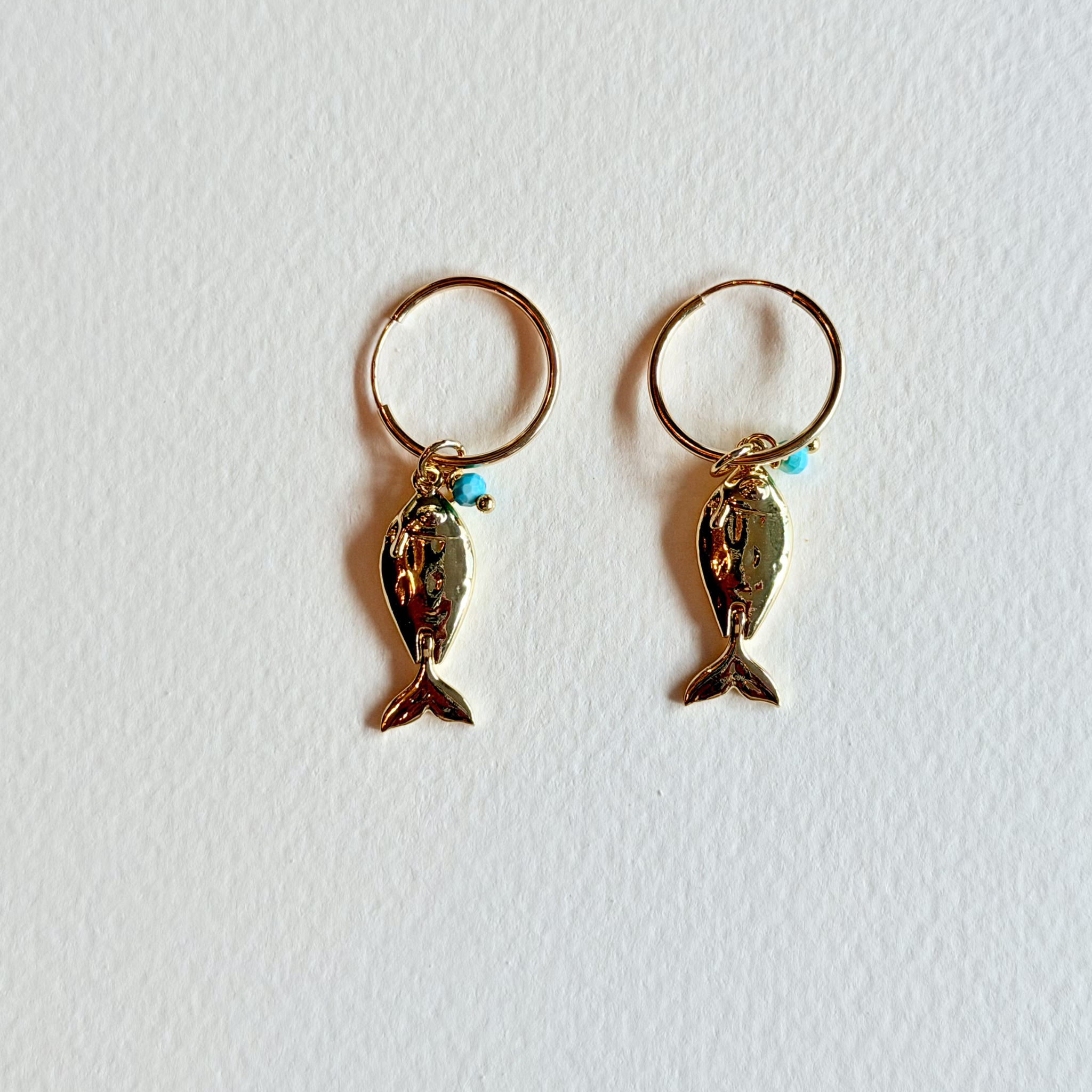 Gold fish-shaped earrings with turquoise beads on a white background