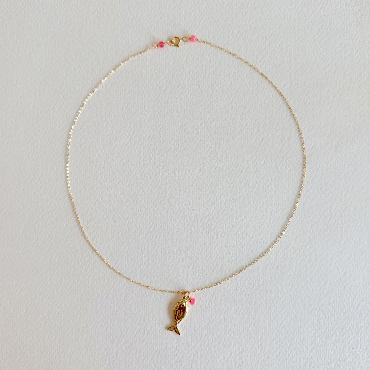 Gold necklace with a fish pendant on a light gray background