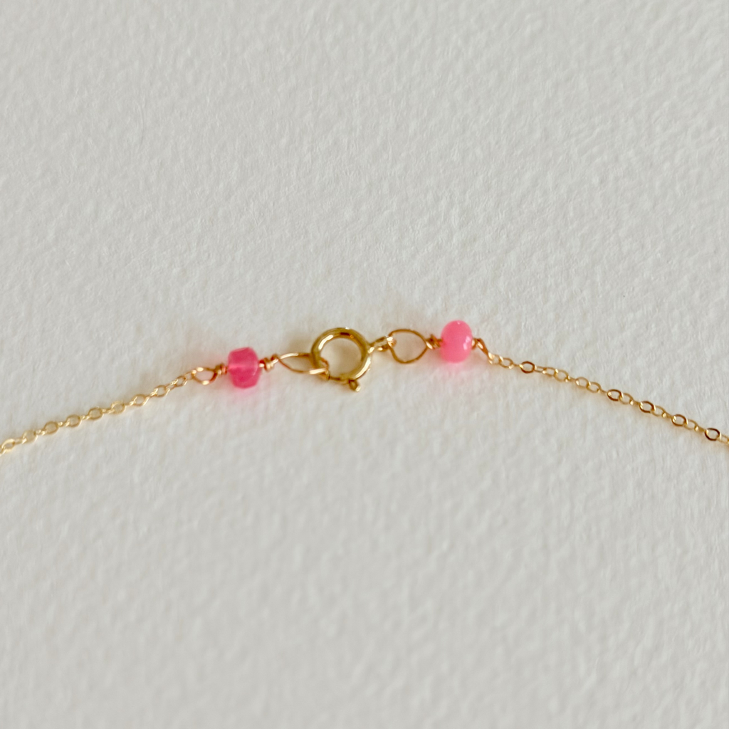 Gold bracelet with pink beads on a light gray background