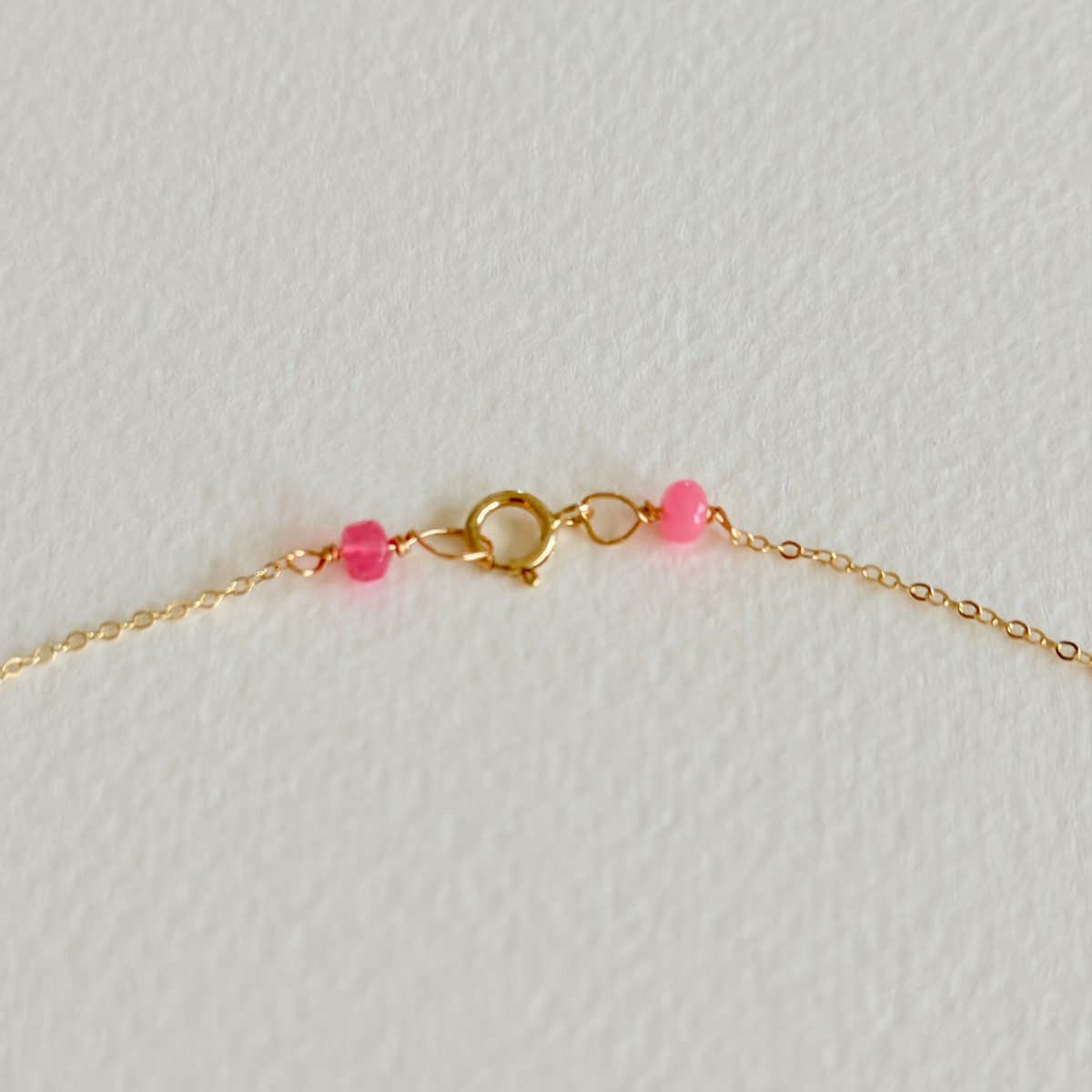 Gold bracelet with pink beads on a light gray background