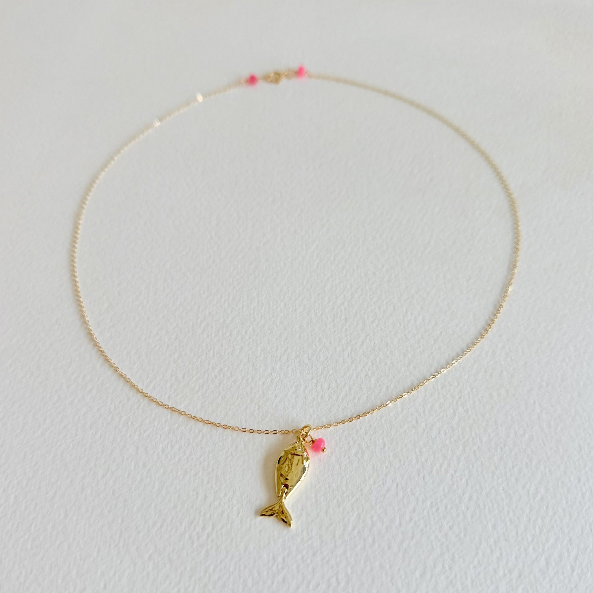 Gold necklace with a fish pendant on a light gray background