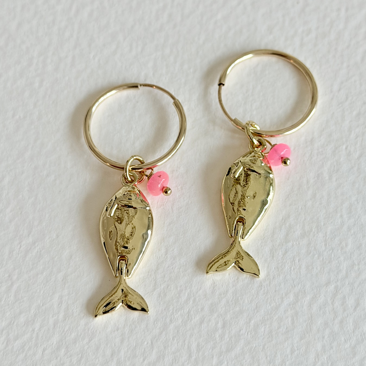 Gold fish-shaped earrings with pink beads on a white background