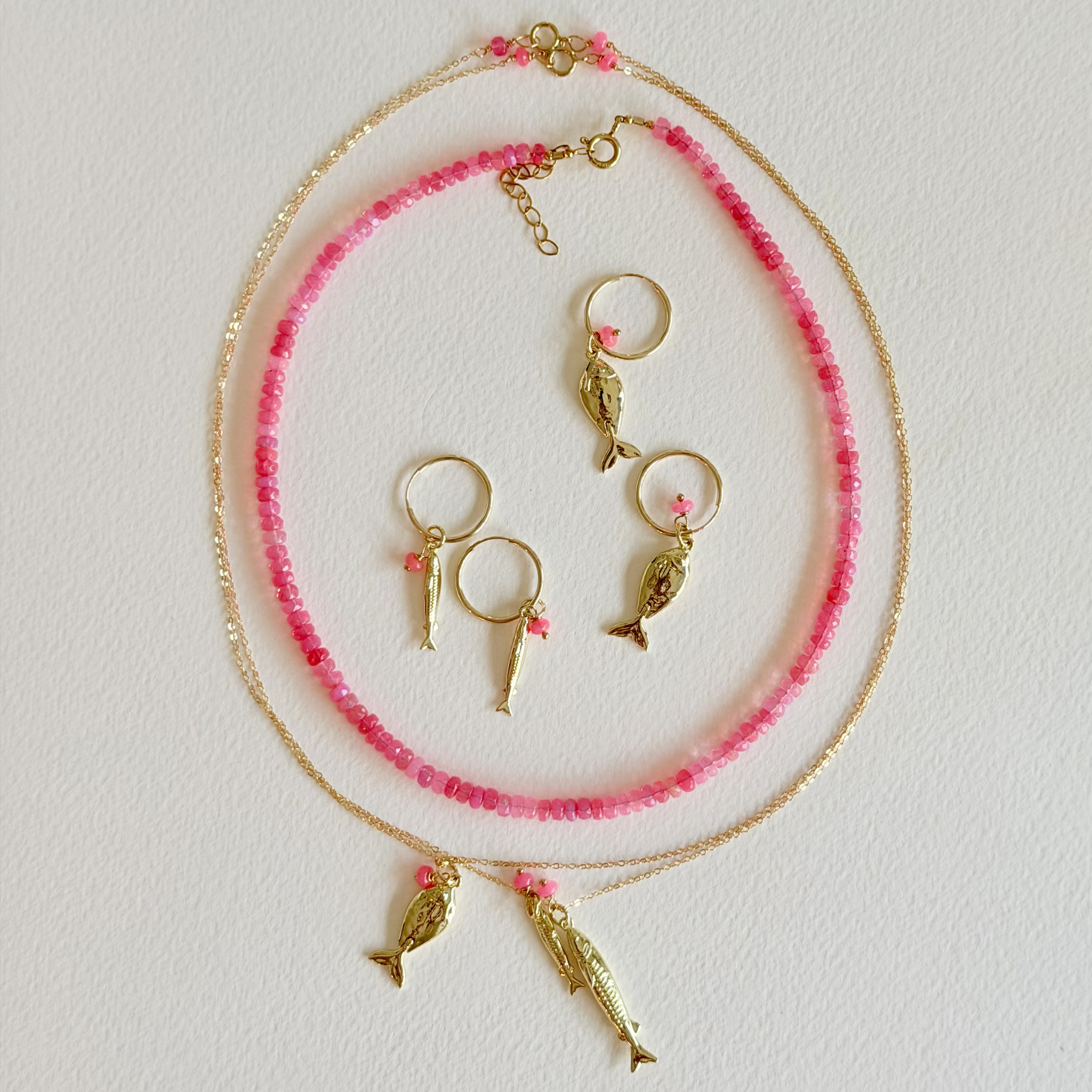 Necklace with pink beads and gold fish charms on a light gray background
