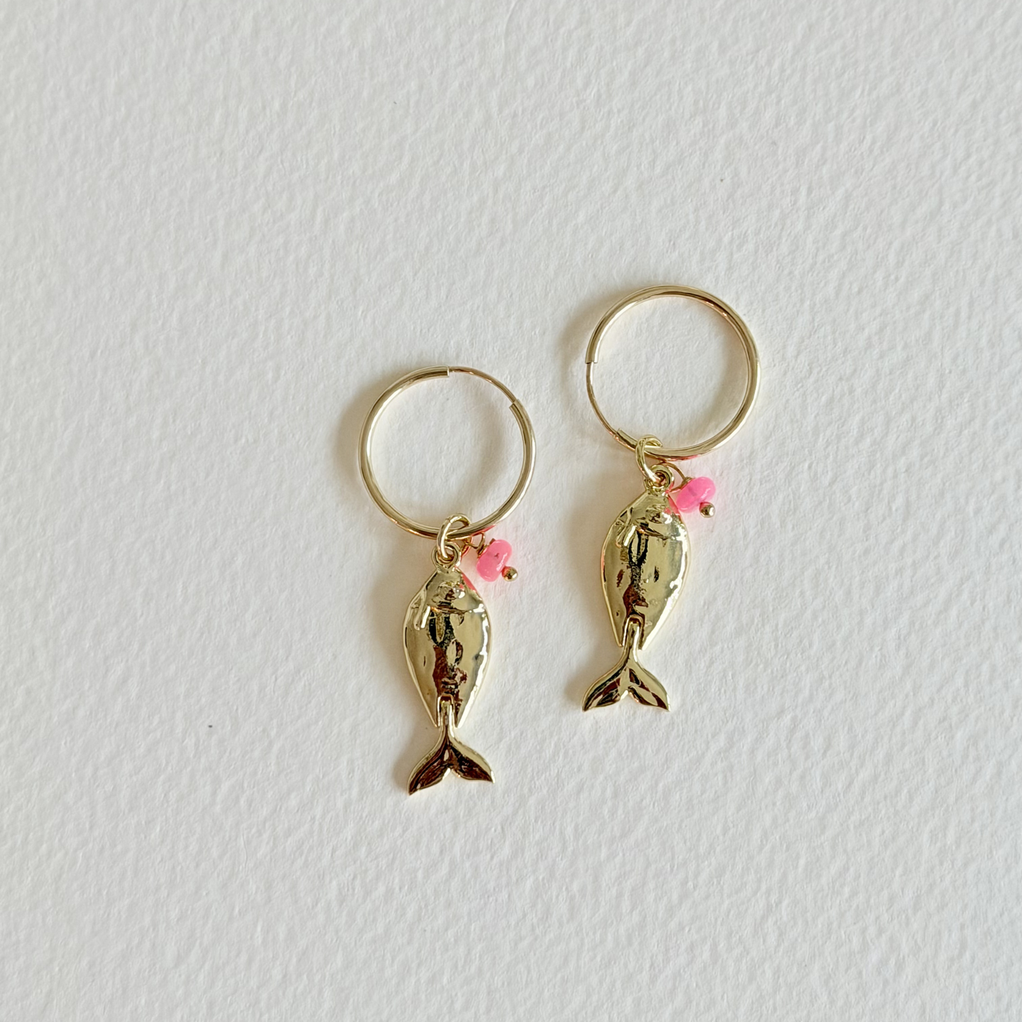 Gold fish-shaped earrings with pink accents on a light gray background