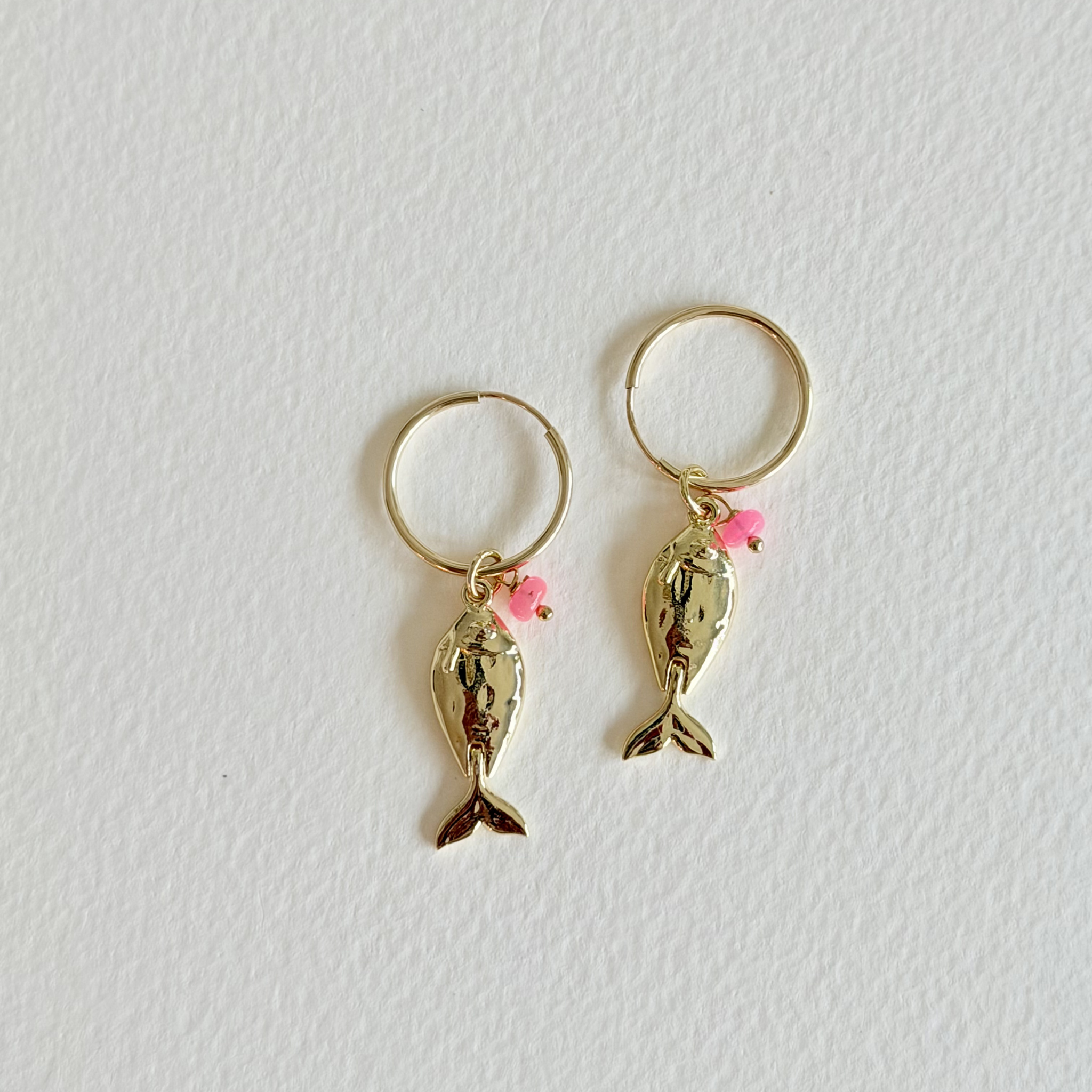 Gold fish-shaped earrings with pink accents on a light gray background