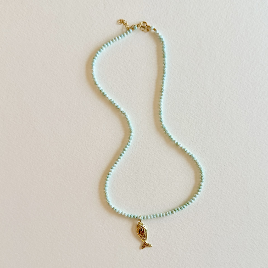 Handmade aqua turquoise beaded necklace with a signature gold fish charm and 14k gold-filled clasp, measuring 16 inches with a 2-inch extender. Inspired by the colors of the sea and handcrafted by Marie & Oakley.