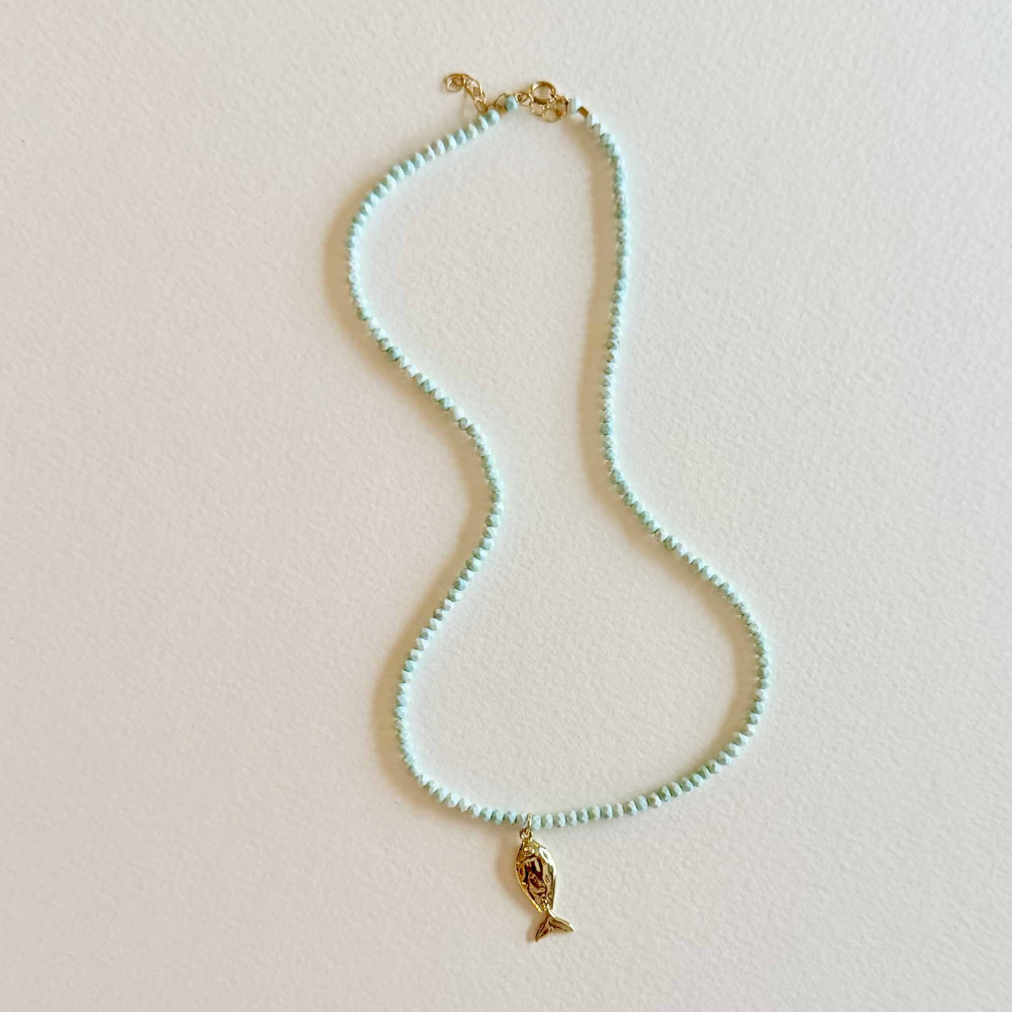 Handmade aqua turquoise beaded necklace with a signature gold fish charm and 14k gold-filled clasp, measuring 16 inches with a 2-inch extender. Inspired by the colors of the sea and handcrafted by Marie & Oakley.