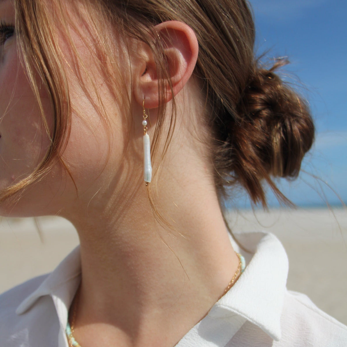 Close-up of a person wearing earrings with a blurred beach background