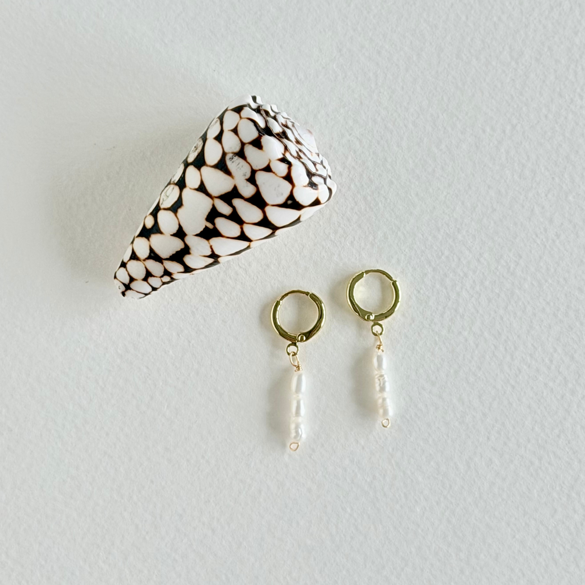 Pair of gold earrings with pearl drops on a light gray background