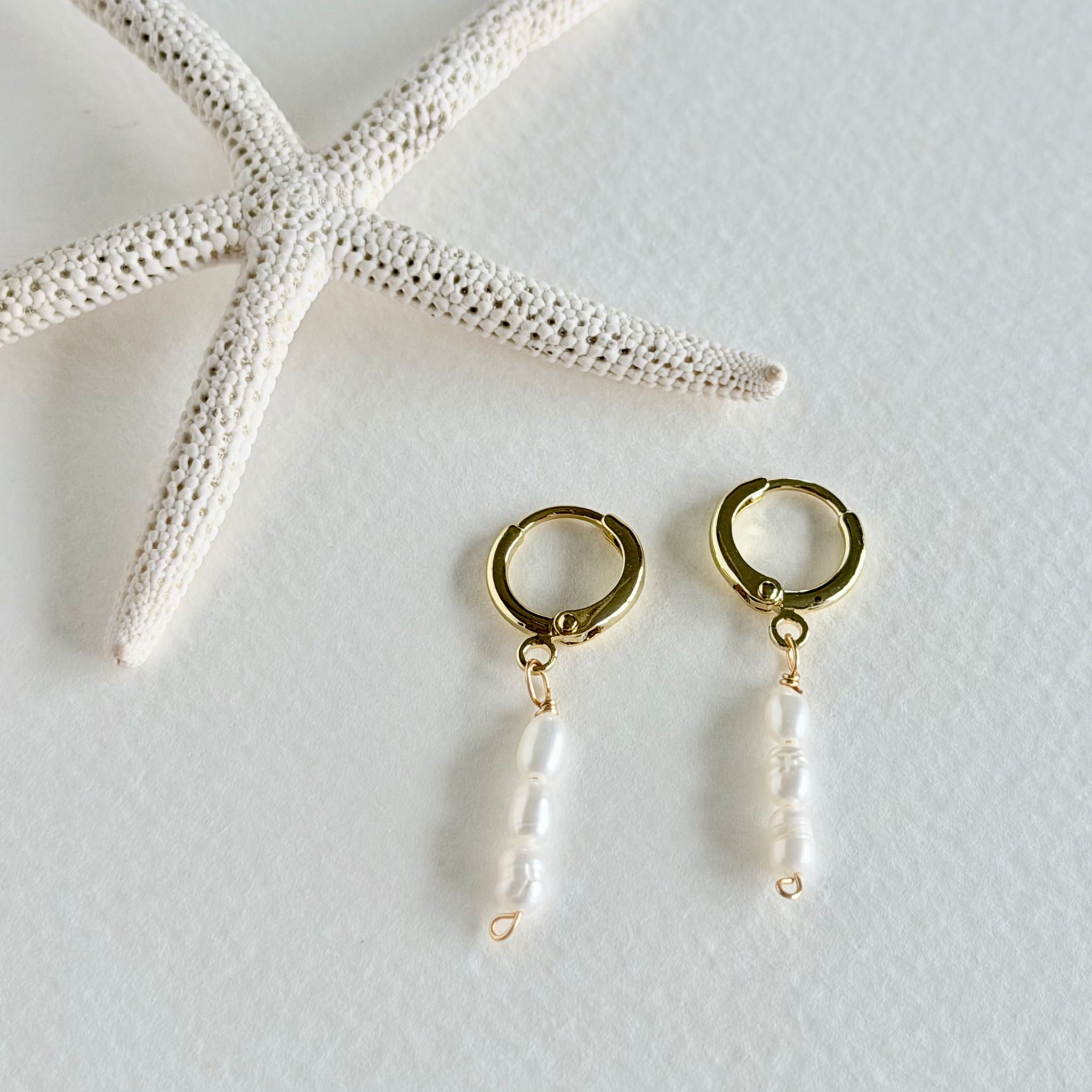 Gold hoop earrings with pearl drops on a light gray background with a starfish.
