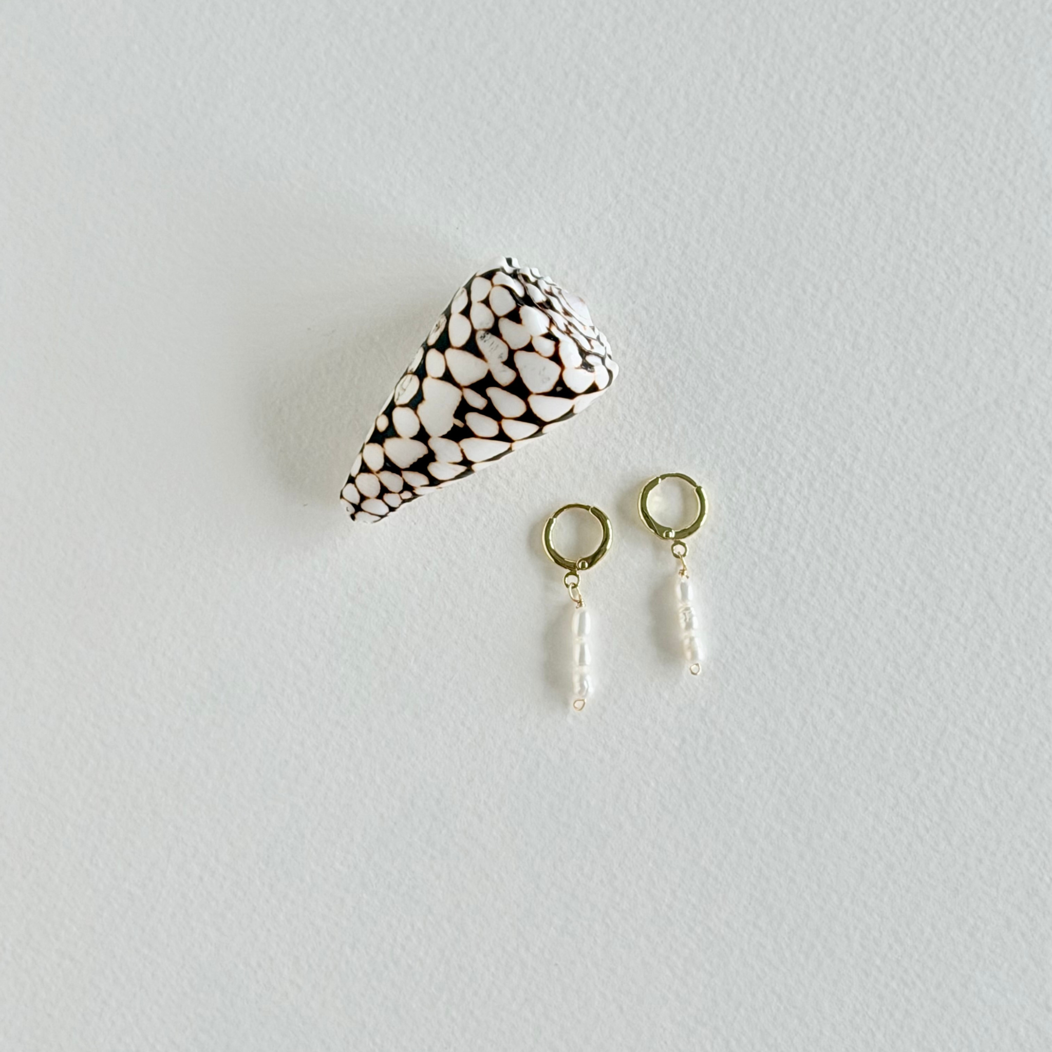 Pair of gold earrings with white beads on a light gray background