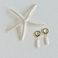 Gold hoop earrings with pearl drops next to a starfish on a light gray background
