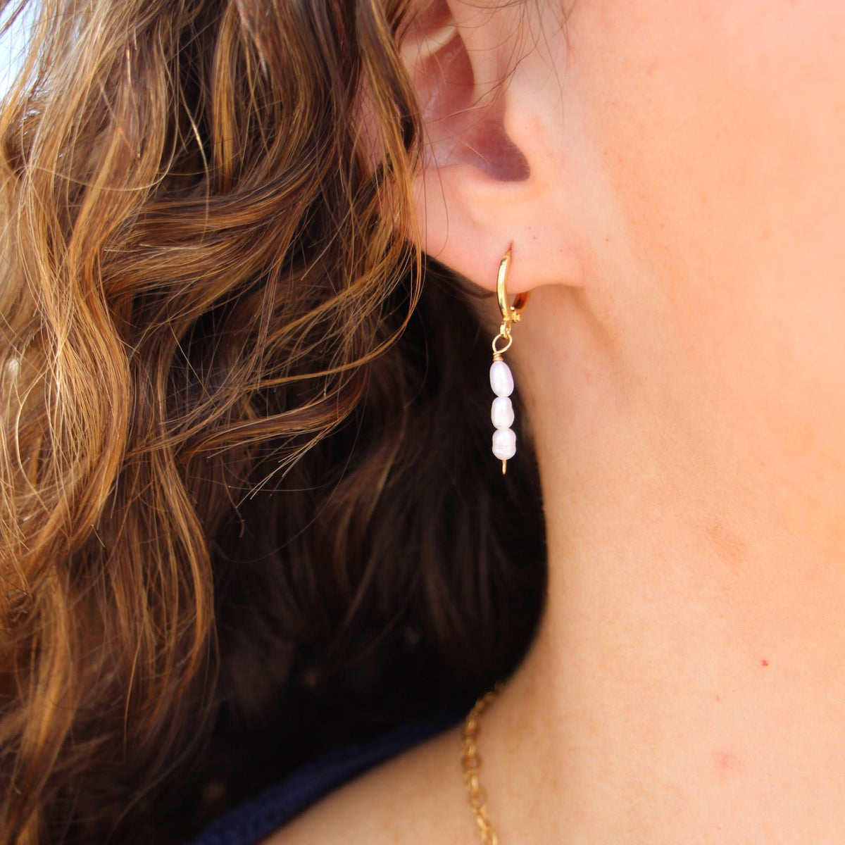 Close-up of a person wearing gold earrings and a necklace with a blurred background