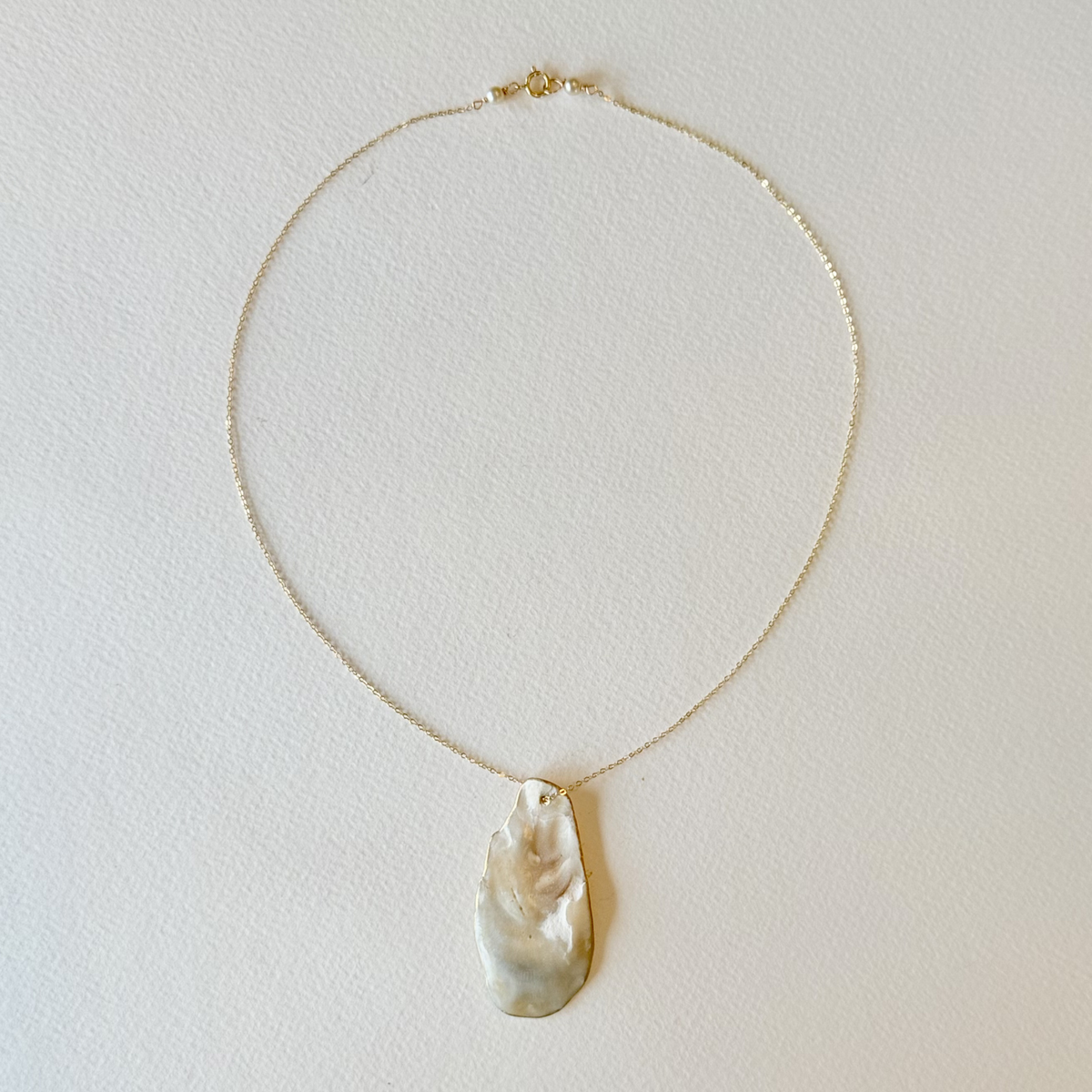 Gold necklace with a large pearl pendant on a light gray background