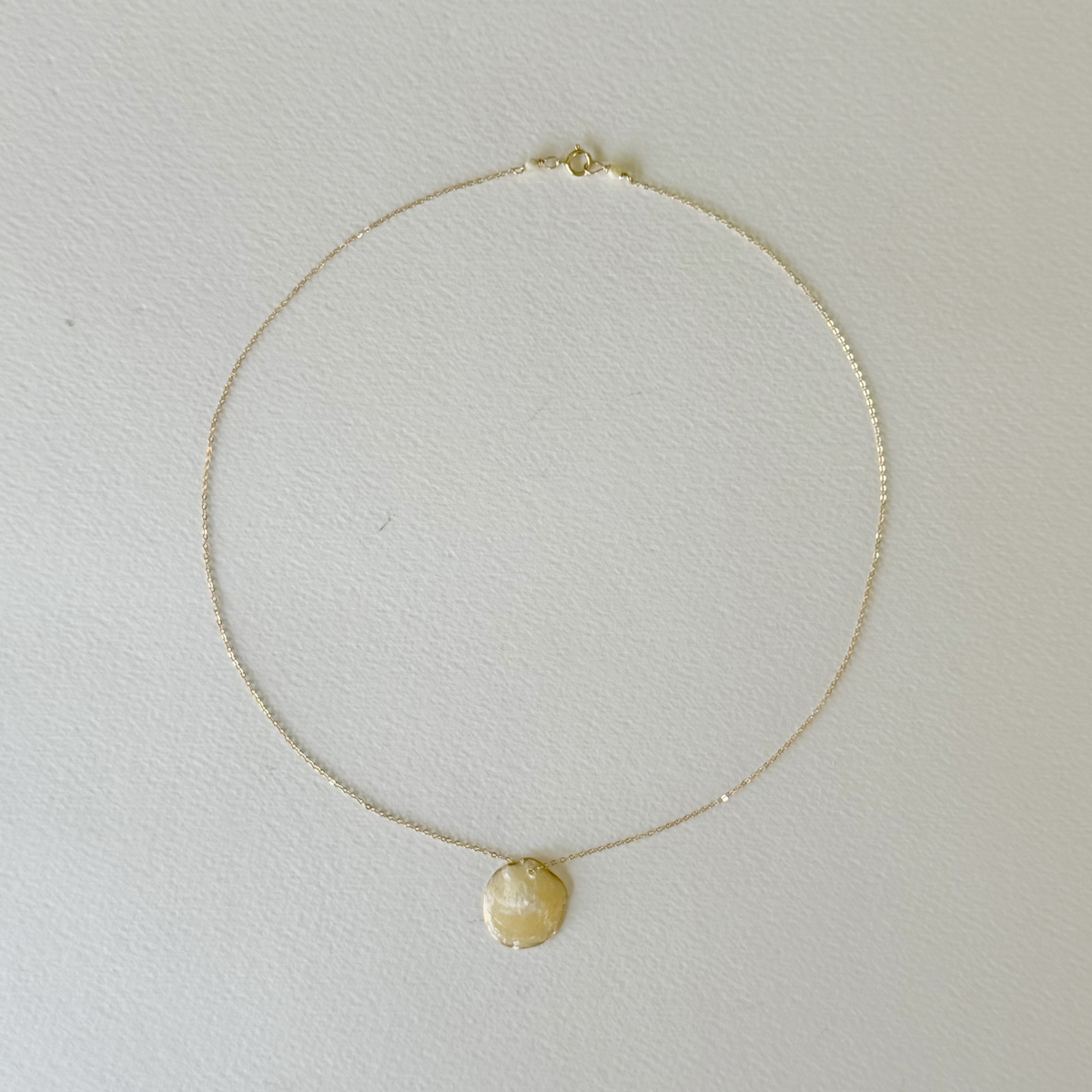 Gold necklace with a round pendant on a light gray background
