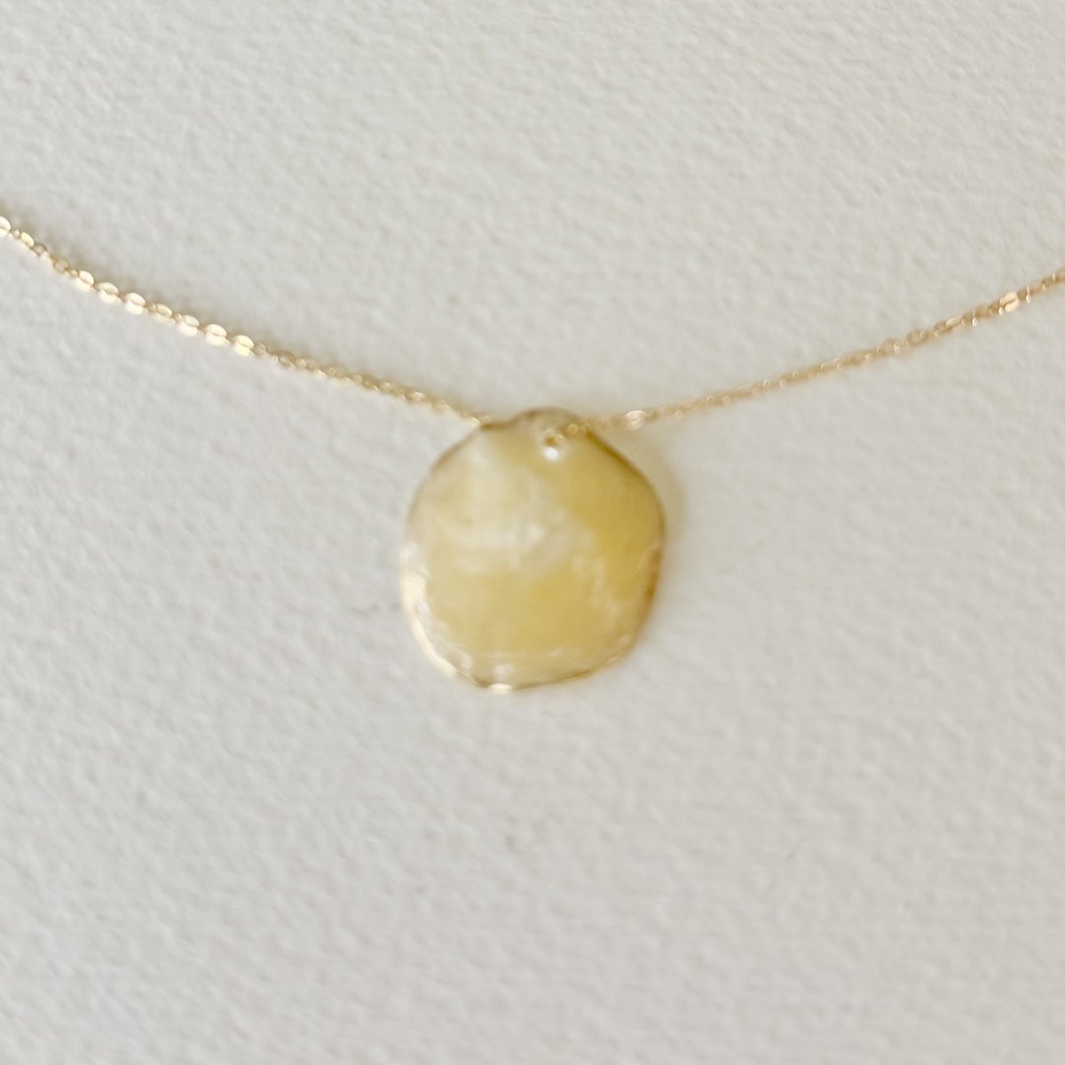 Gold necklace with a round pendant on a light gray background