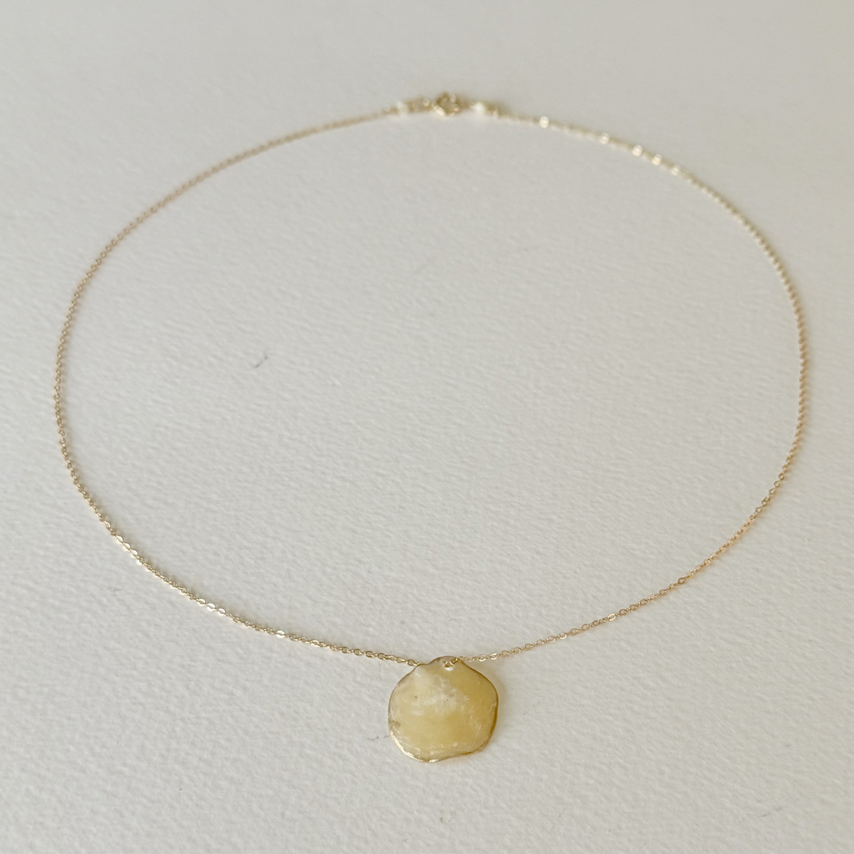 Gold necklace with a round pendant on a light gray background