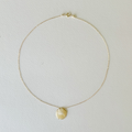 Gold necklace with a round pendant on a light gray background